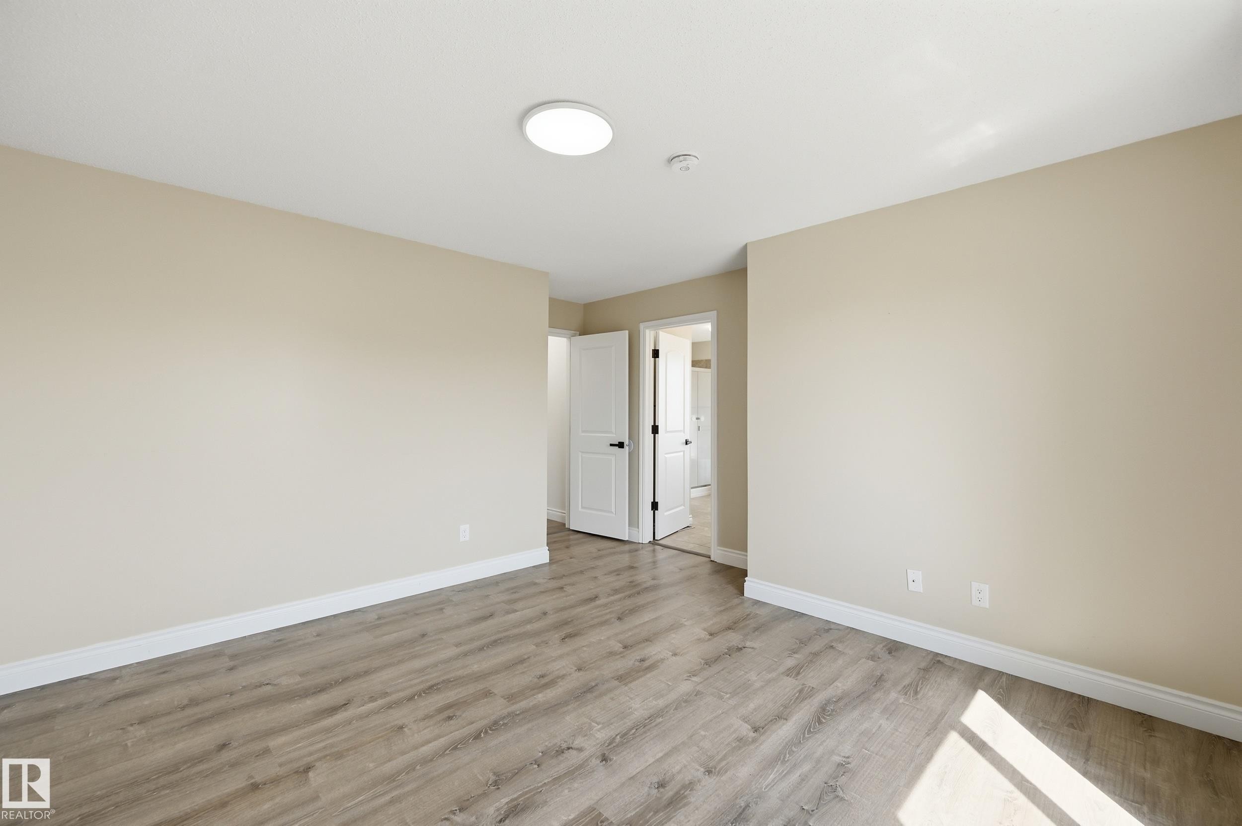Spacious room featuring wood-finish flooring, light neutral wall paint, white trim, and a contemporary flush-mount ceiling light - 1 Southfork Close, Leduc, AB - Indoor Photo Showing Other Room