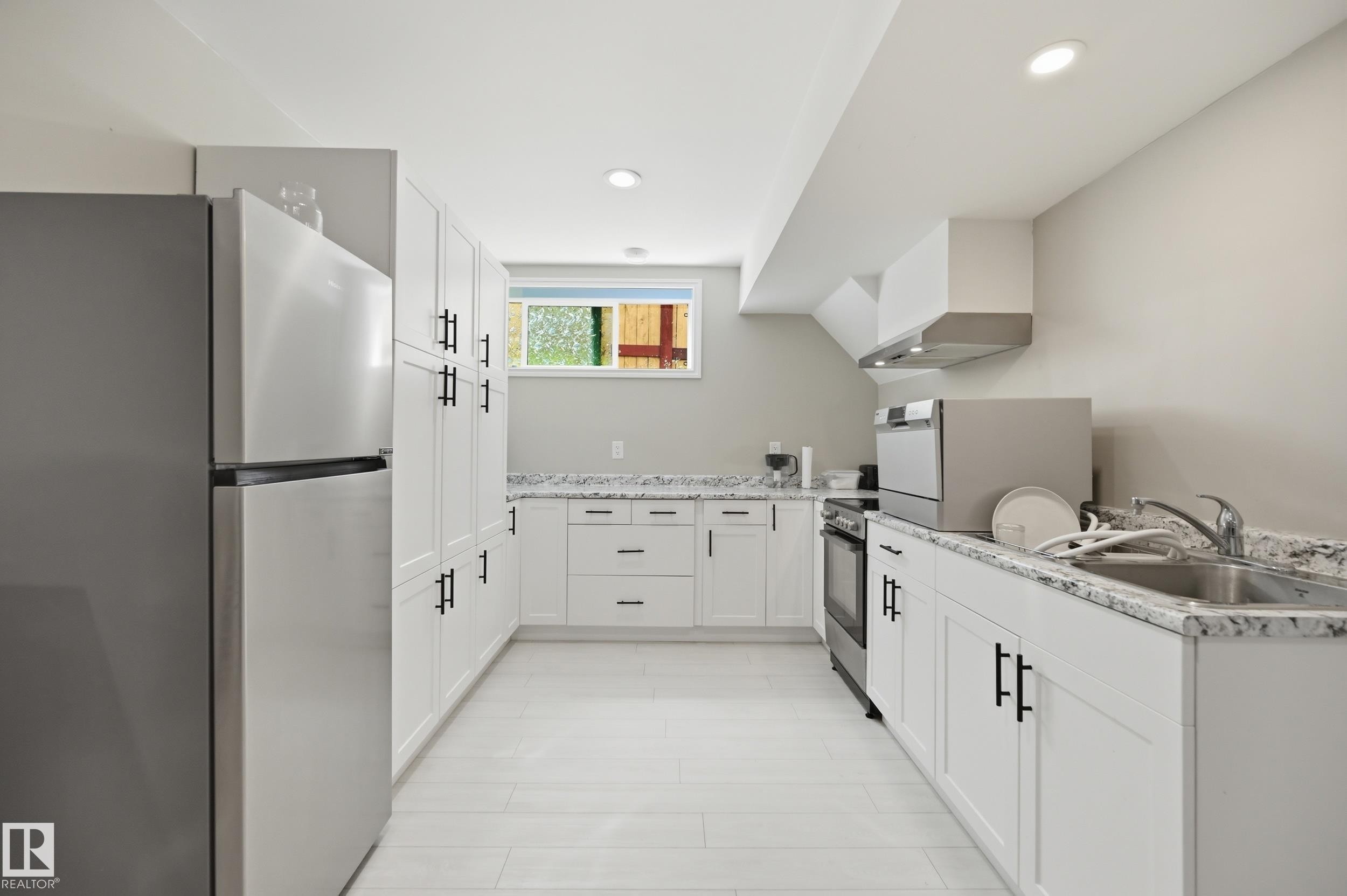Contemporary kitchen featuring white cabinetry with matte black hardware, stainless steel appliances, and light-toned wood-finish flooring - 1 Southfork Close, Leduc, AB - Indoor Photo Showing Kitchen With Double Sink