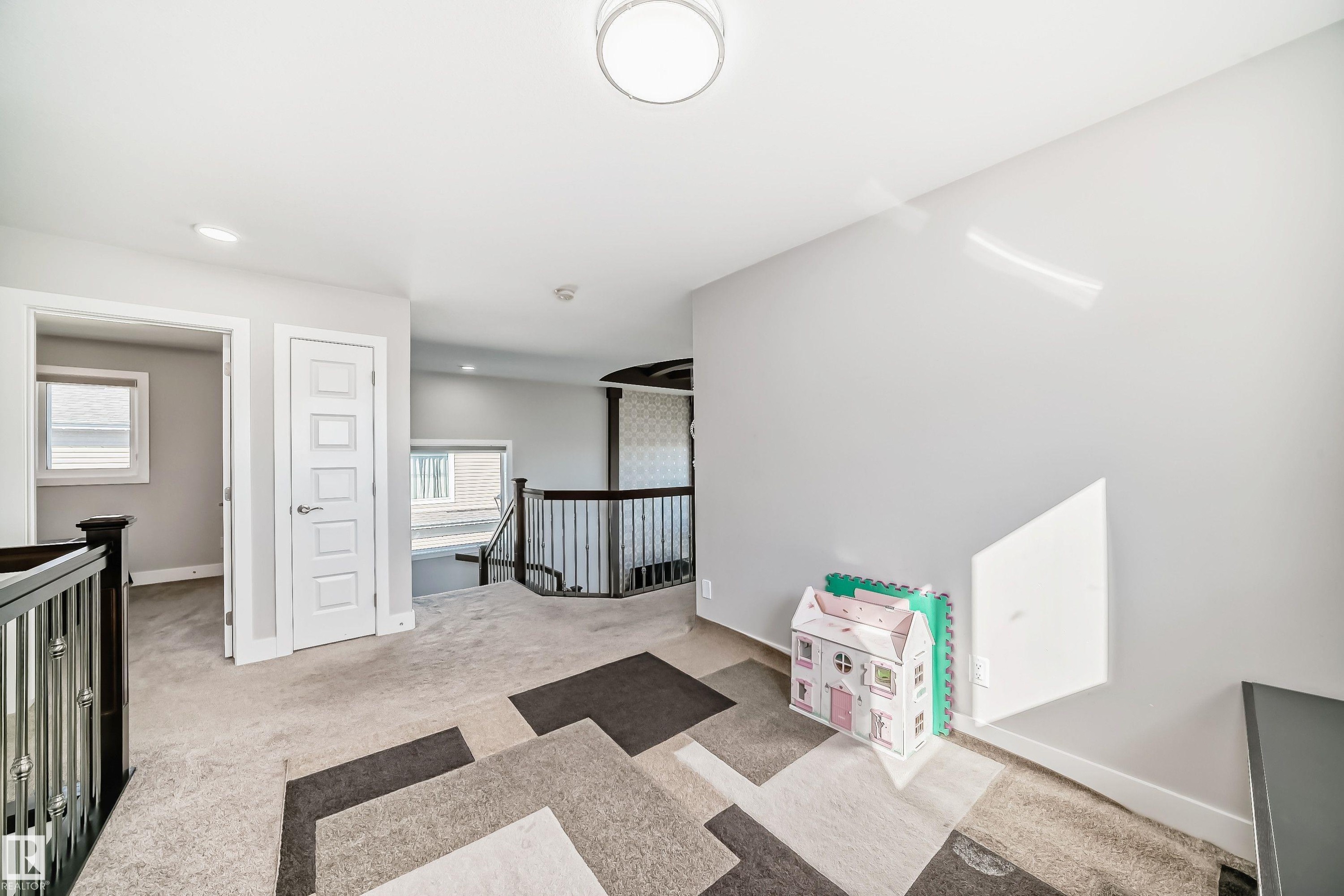Upper-level landing featuring light gray walls, light beige carpet, and a modern geometric area rug - 2464 15 Avenue Nw, Edmonton, AB - Indoor