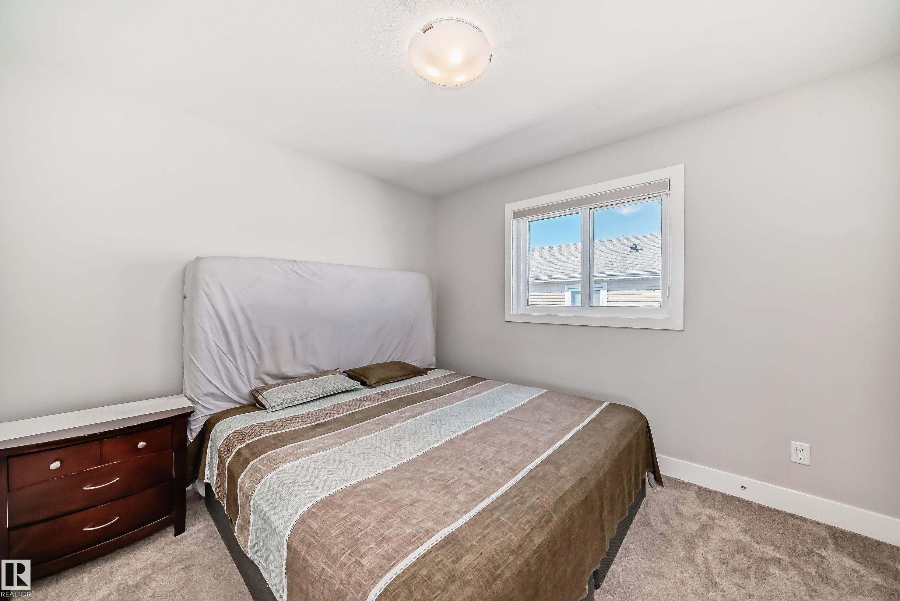 Well-lit bedroom featuring light gray walls, white trim, and a window with white casing - 2464 15 Avenue Nw, Edmonton, AB - Indoor Photo Showing Bedroom