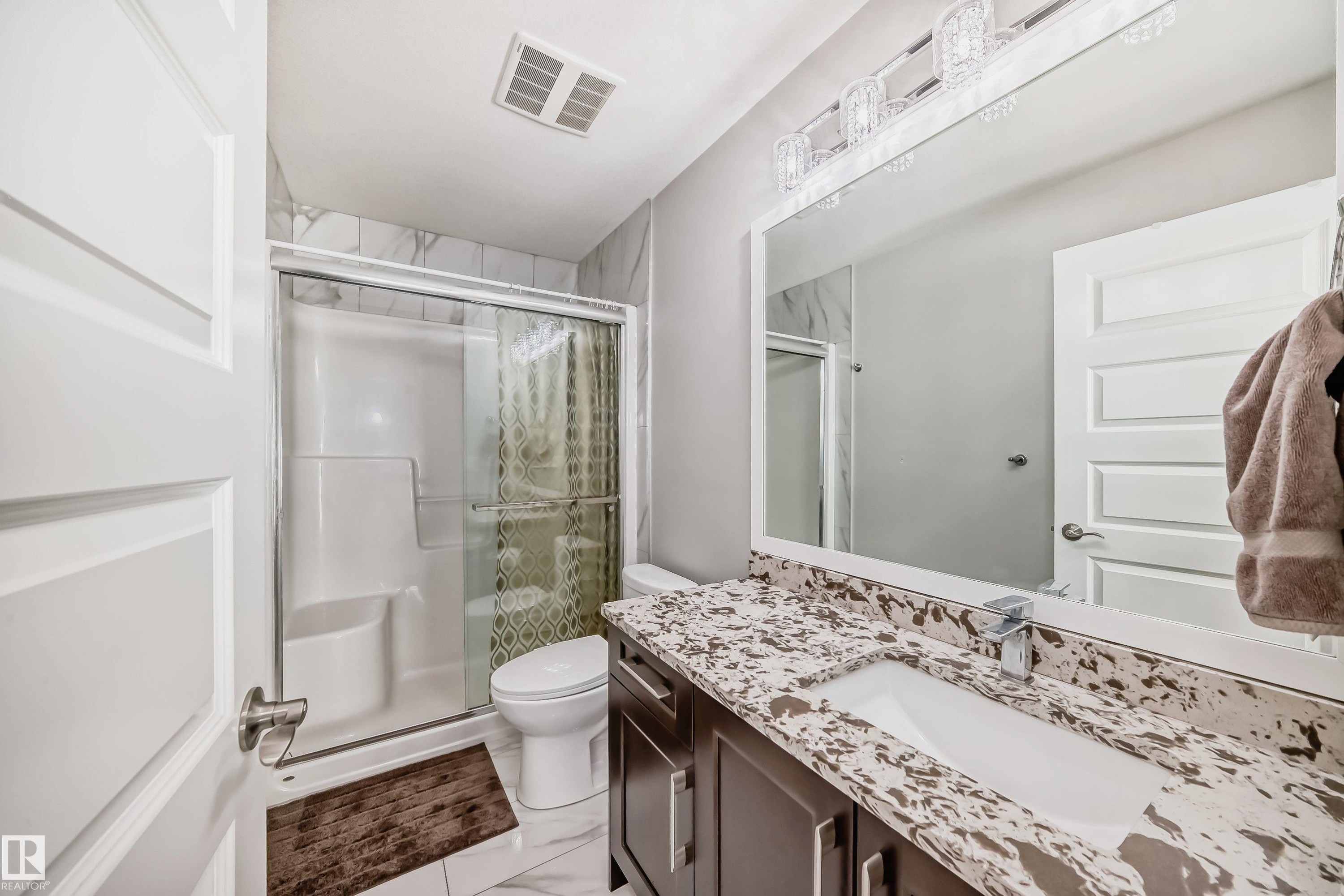 Bathroom featuring a shower with sliding glass doors, a vanity with a white rectangular sink, a speckled countertop, dark wood-finish cabinetry, and a large wall-mounted mirror - 2464 15 Avenue Nw, Edmonton, AB - Indoor Photo Showing Bathroom