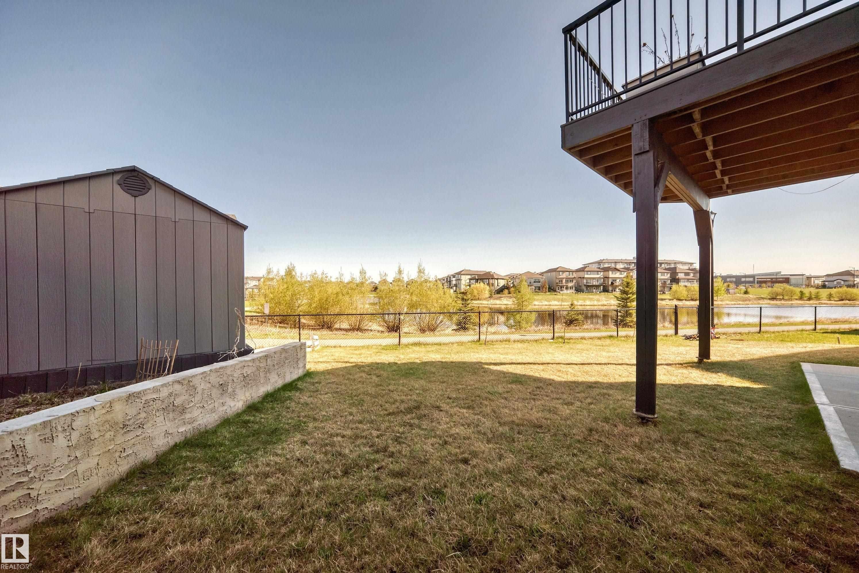 Expansive backyard featuring a metal storage shed, a stucco retaining wall, and a raised wooden deck with black metal railings - 2464 15 Avenue Nw, Edmonton, AB - Outdoor