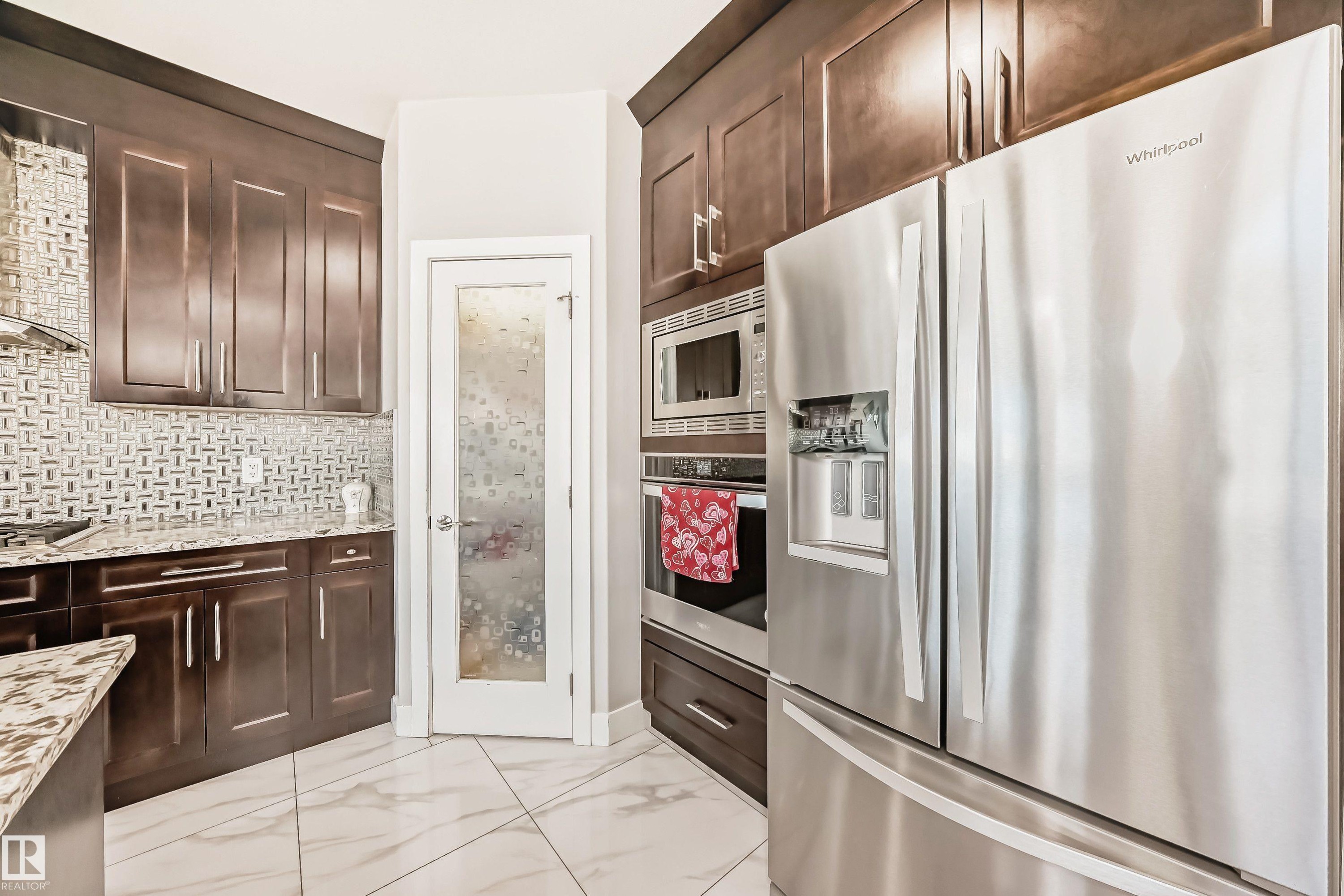 Modern kitchen featuring dark wood cabinetry, stainless steel appliances, and a mosaic tile backsplash - 2464 15 Avenue Nw, Edmonton, AB - Indoor Photo Showing Kitchen