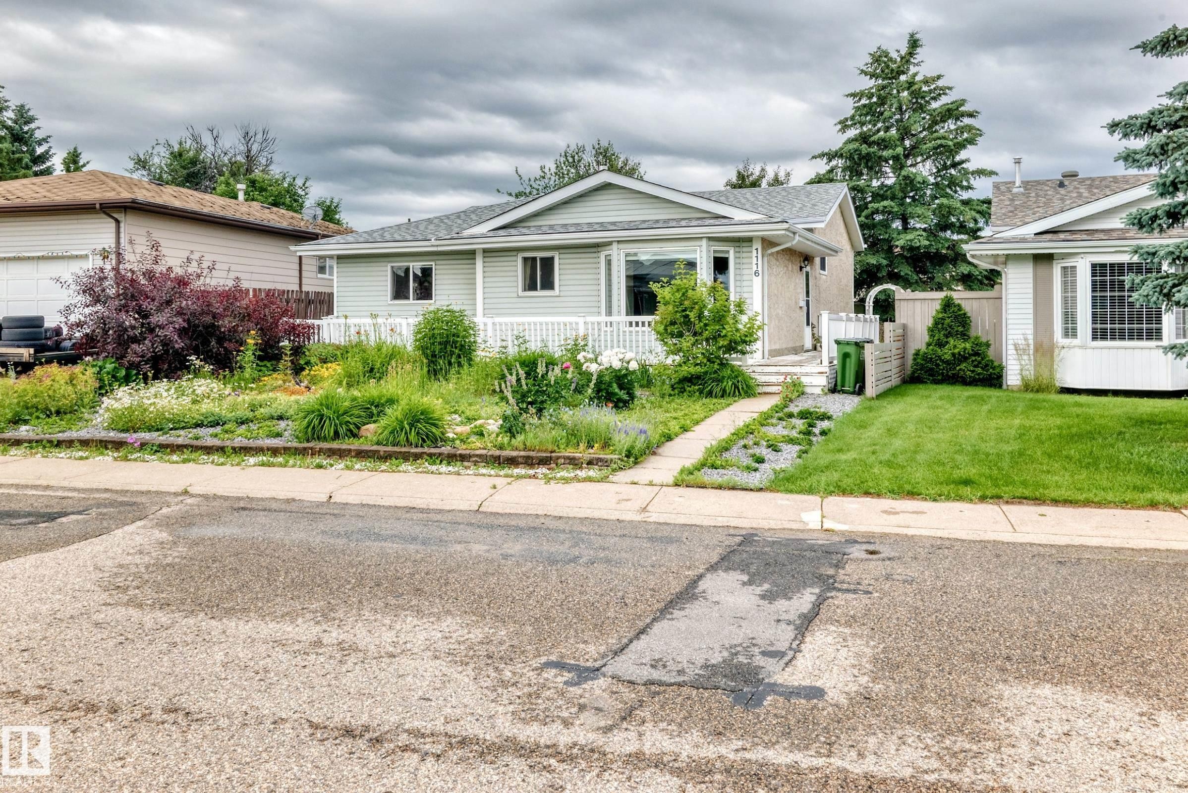 Light blue siding exterior featuring a white porch railing, front yard landscaping, a concrete walkway, and a manicured lawn - 1116 39 Street Nw, Edmonton, AB - Outdoor