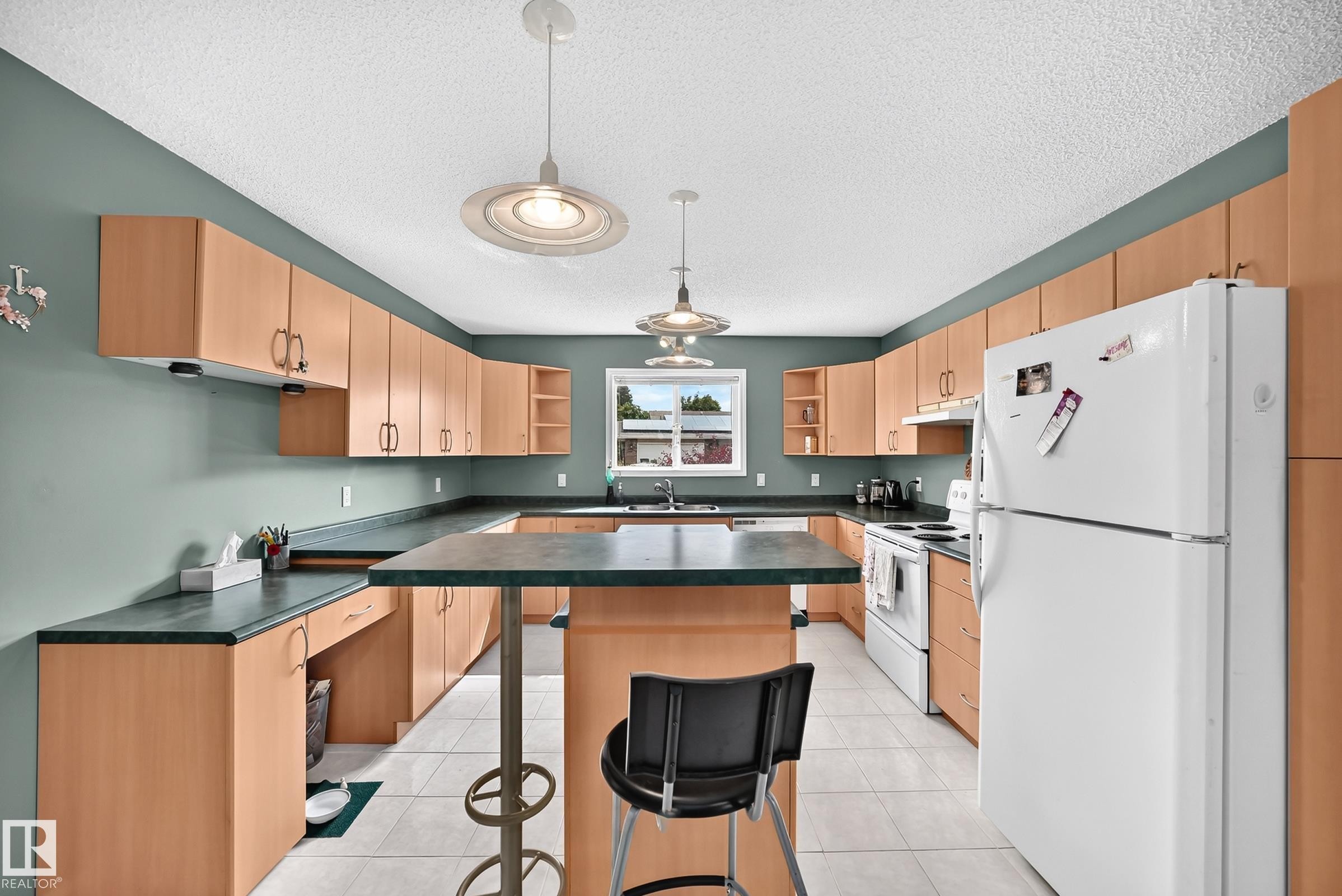 Kitchen featuring extensive light wood-finish cabinetry, dark countertops, white appliances, and tiled flooring - 1116 39 Street Nw, Edmonton, AB - Indoor Photo Showing Kitchen With Double Sink