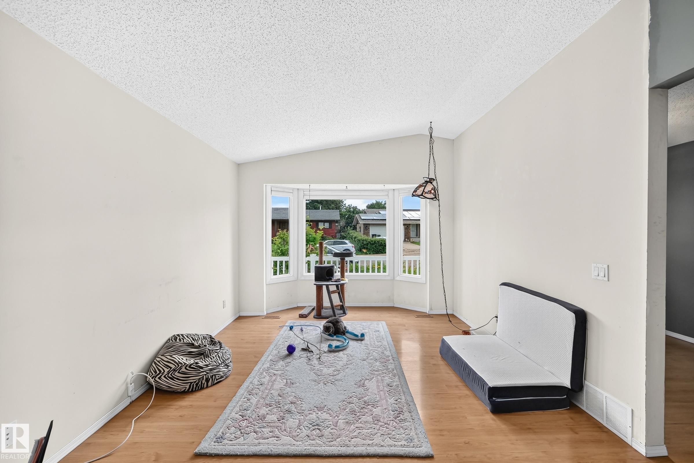 Bright living area featuring a bay window with white trim, wood-finish flooring, neutral wall tones, and a textured ceiling - 1116 39 Street Nw, Edmonton, AB - Indoor