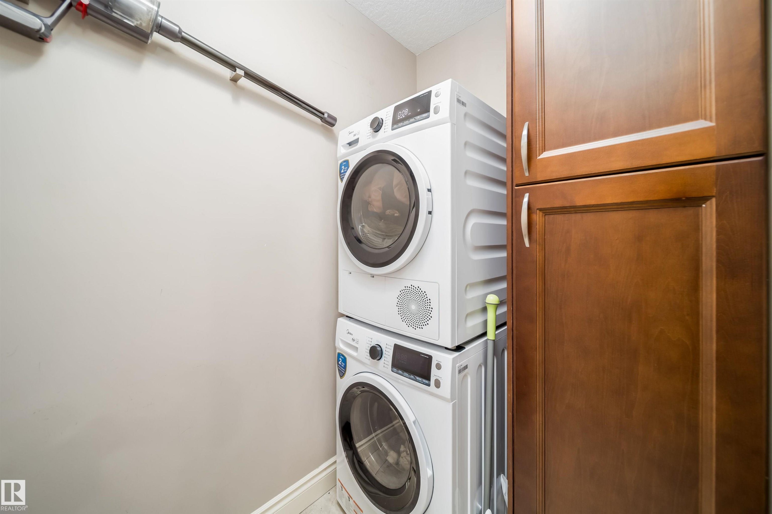 Dedicated laundry area featuring stacked front-loading appliances and adjacent built-in cabinetry with panel doors and brushed nickel hardware - 11342 79 Avenue, Edmonton, AB - Indoor Photo Showing Laundry Room