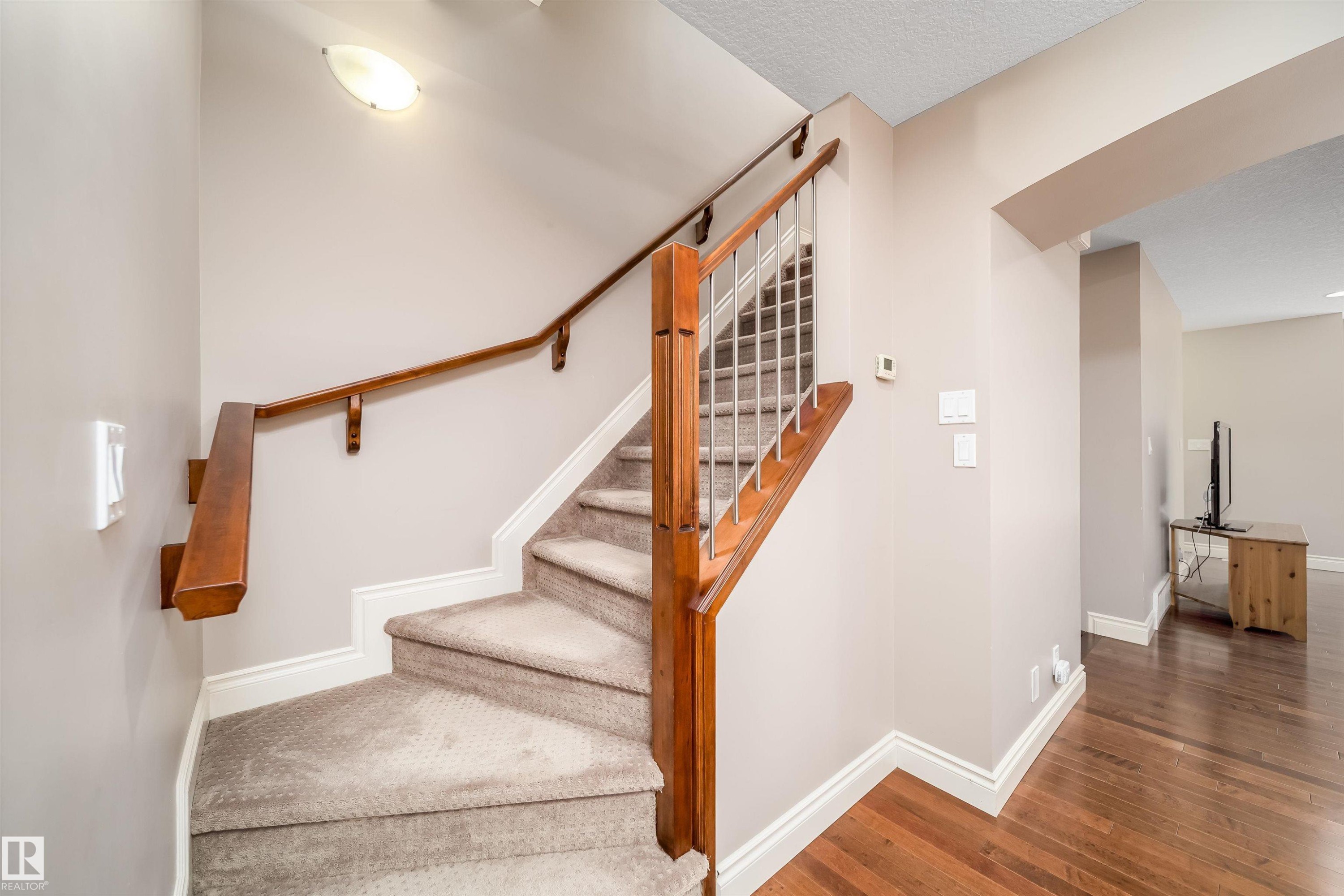 Carpeted staircase featuring a wood handrail with metal balusters - 11342 79 Avenue, Edmonton, AB - Indoor Photo Showing Other Room