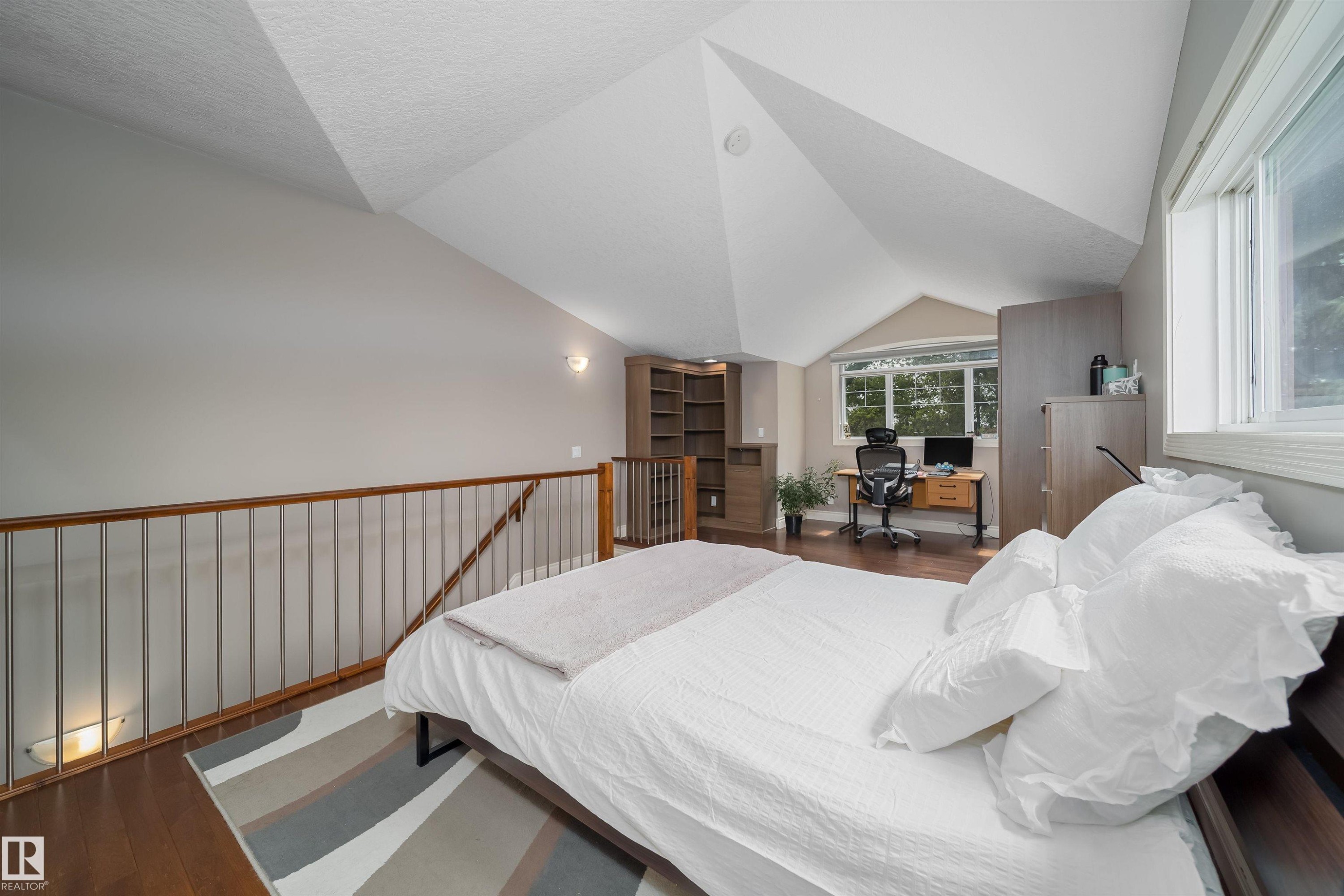 Spacious loft area featuring sloped ceilings, wood-finish flooring, and a contemporary railing with metal spindles - 11342 79 Avenue, Edmonton, AB - Indoor Photo Showing Bedroom