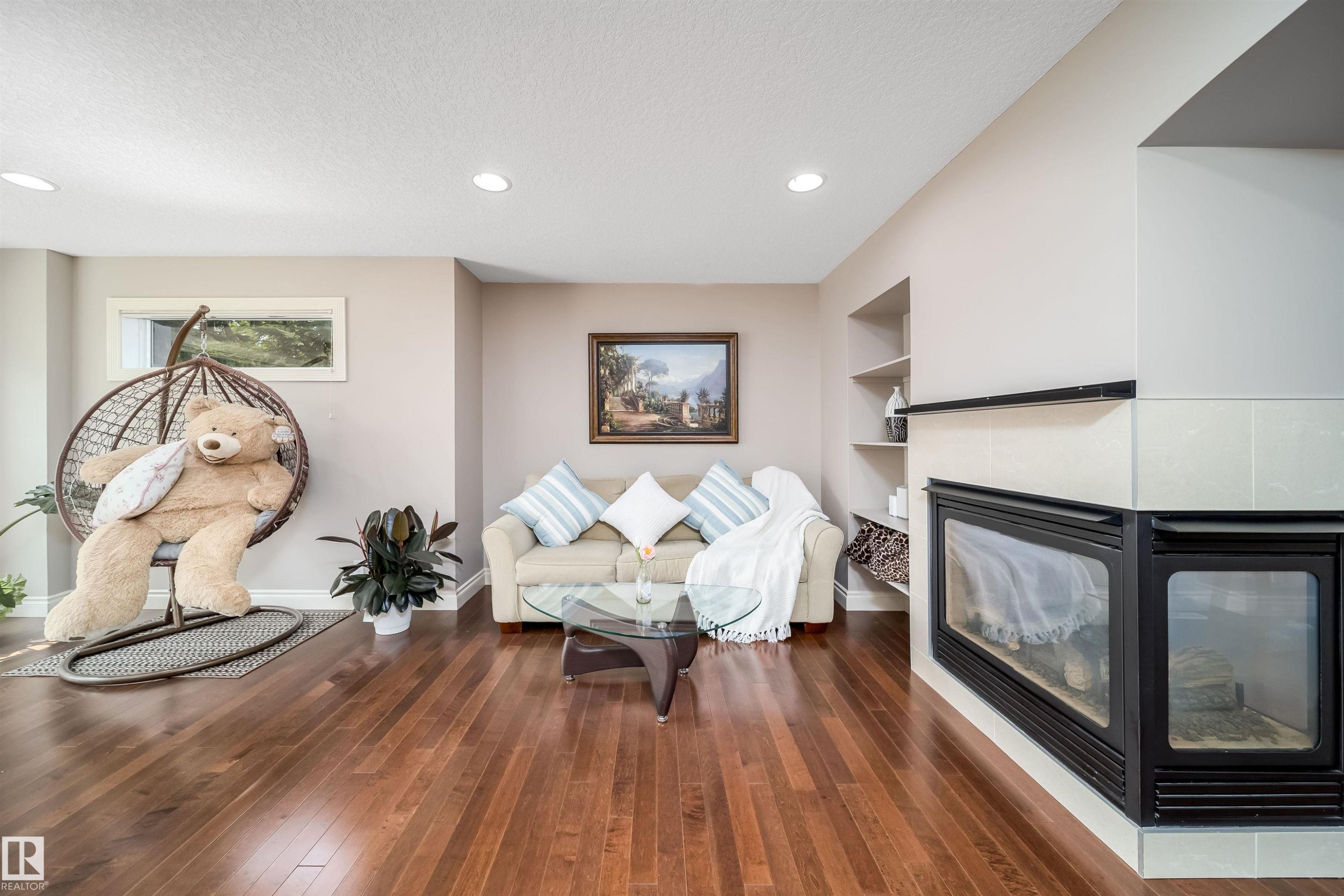 Living area featuring warm wood-finish flooring, recessed lighting, and a corner fireplace with a tiled surround - 11342 79 Avenue, Edmonton, AB - Indoor Photo Showing Other Room With Fireplace