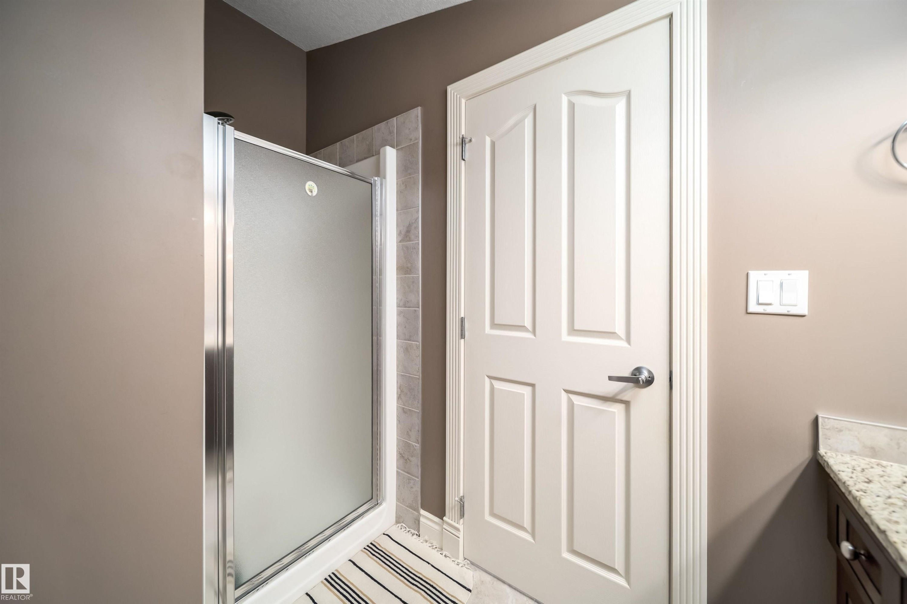 Shower enclosure with frosted glass panels, tile surround, and a white paneled door - 11342 79 Avenue, Edmonton, AB - Indoor