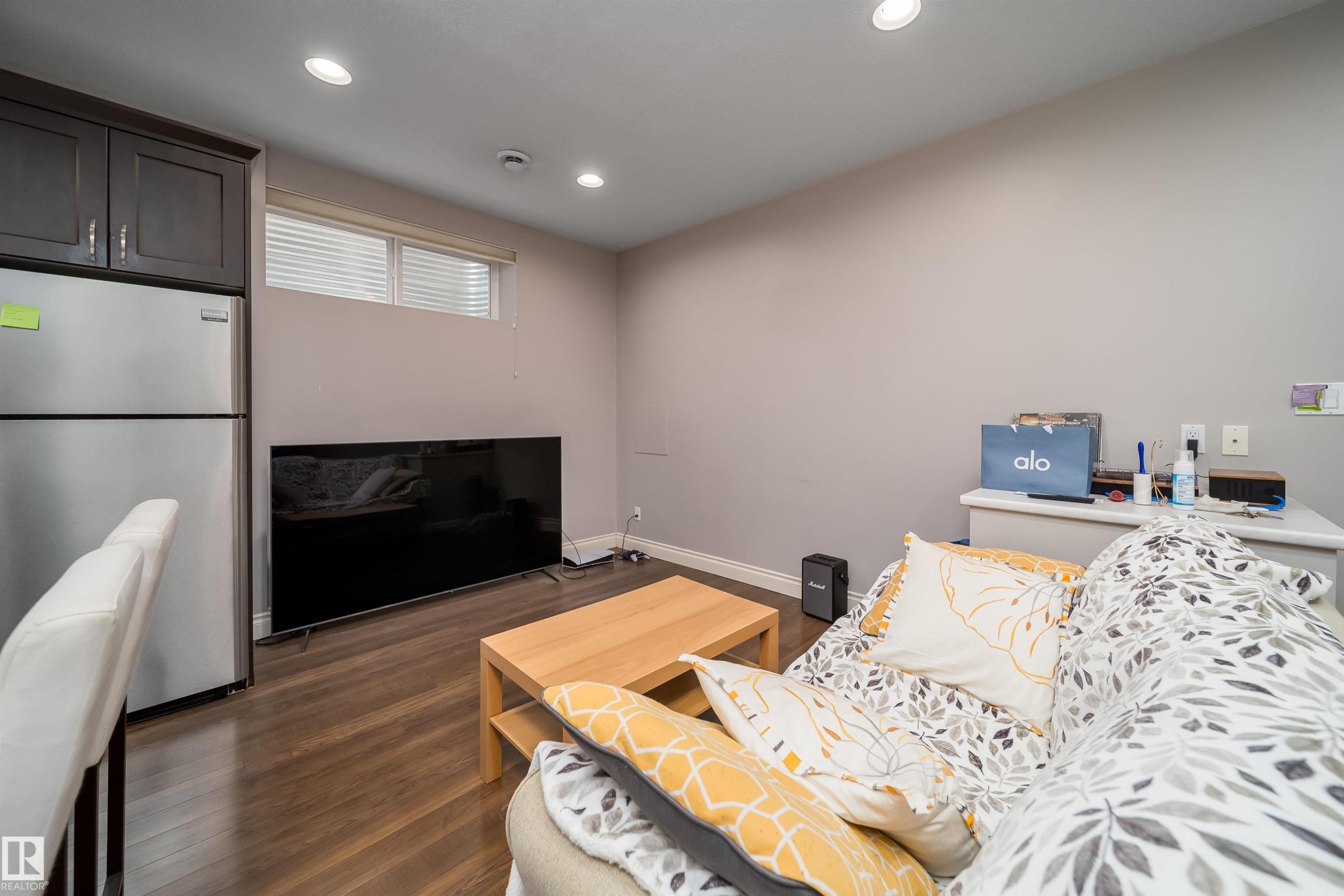 Living area featuring wood-finish flooring, recessed lighting, and a stainless steel refrigerator with dark cabinetry - 11342 79 Avenue, Edmonton, AB - Indoor
