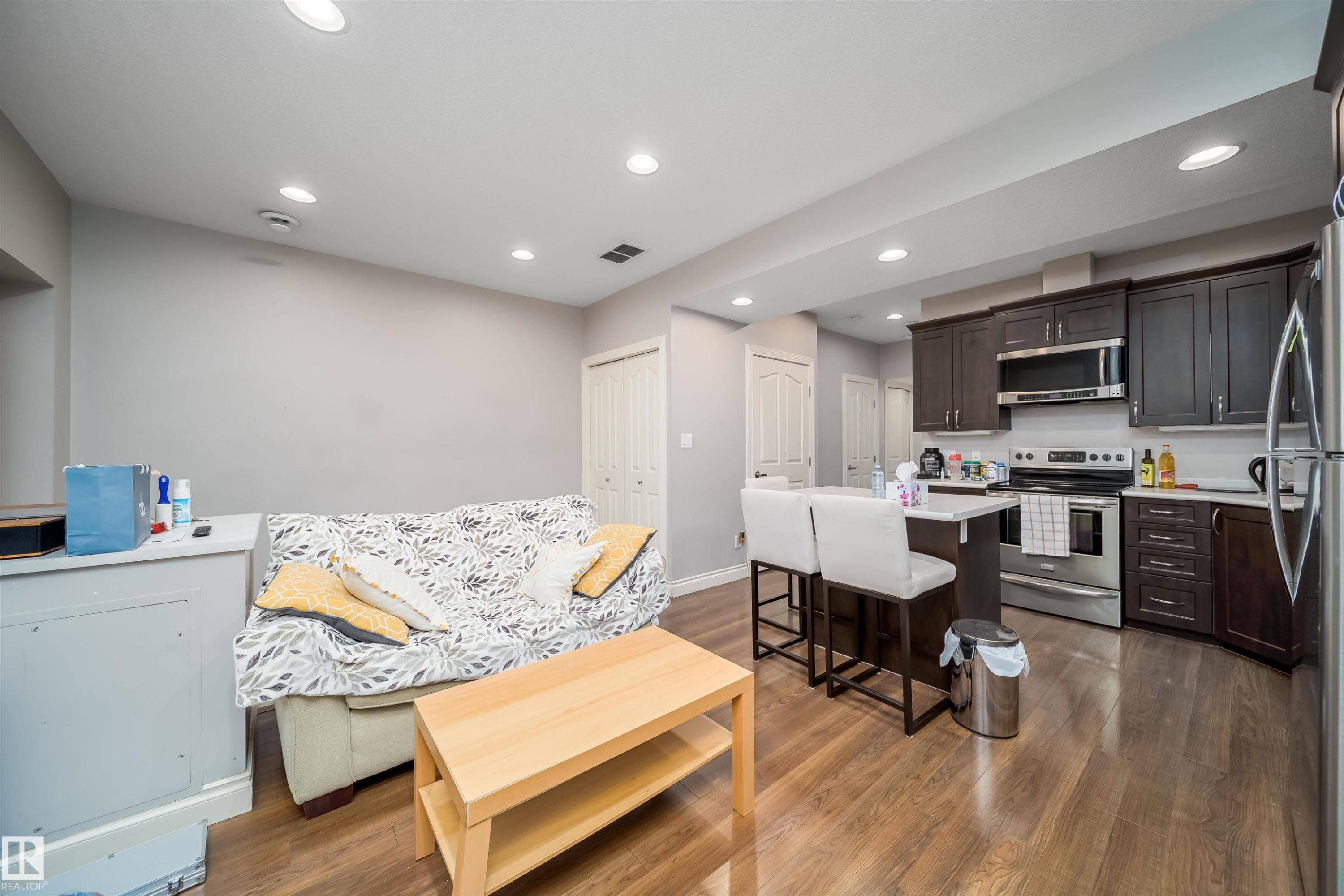 Open-concept living area featuring wood-finish flooring, recessed lighting, and a kitchen with dark wood cabinetry - 11342 79 Avenue, Edmonton, AB - Indoor Photo Showing Kitchen