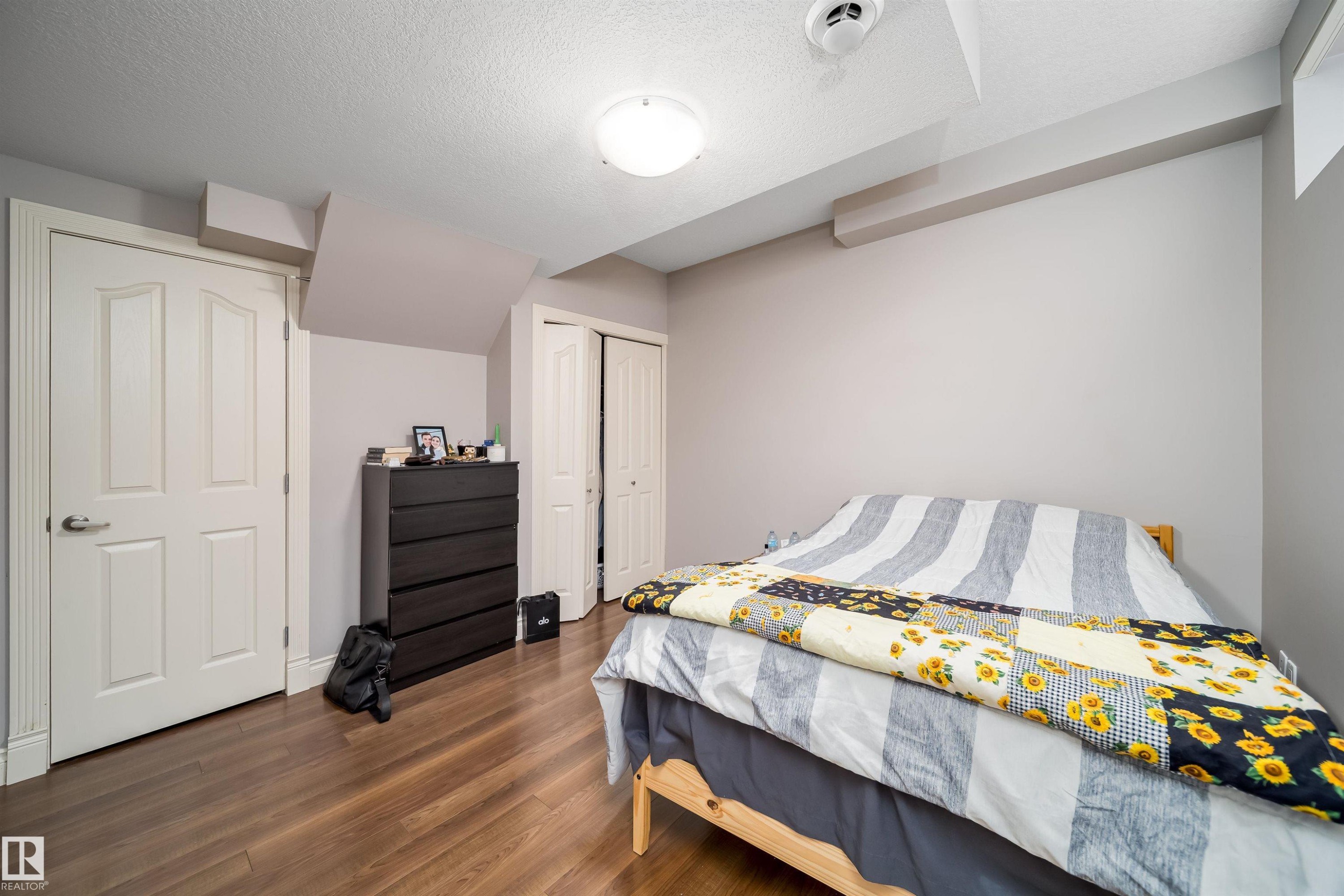 Spacious room featuring wood-finish flooring, light grey painted walls, a white flush-mount ceiling light, and a bi-fold closet door - 11342 79 Avenue, Edmonton, AB - Indoor Photo Showing Bedroom