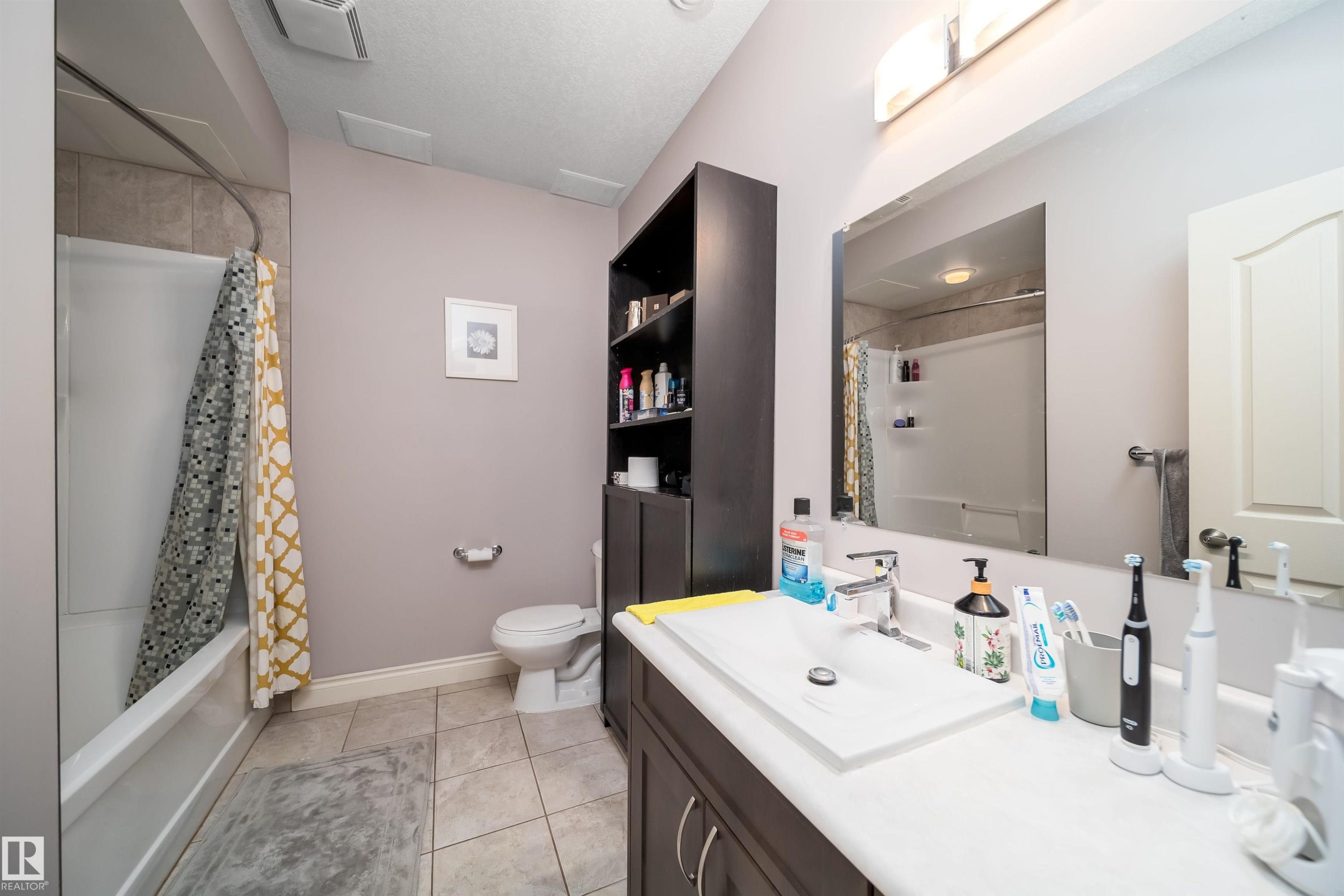 Bathroom featuring a white vanity with an integrated sink, a large wall-mounted mirror, a tub-shower combination with tiled surround, and tiled flooring - 11342 79 Avenue, Edmonton, AB - Indoor Photo Showing Bathroom