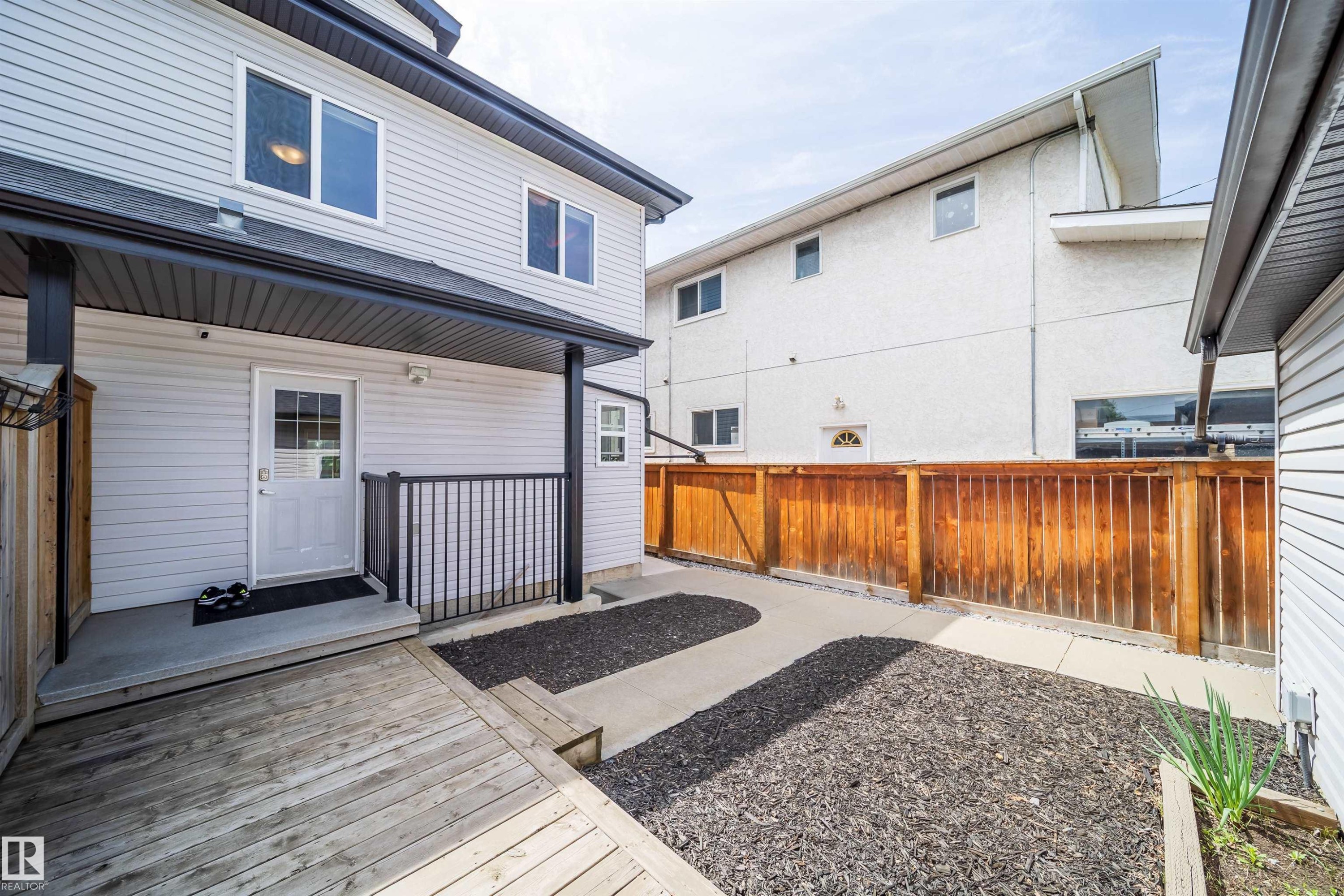 Rear exterior featuring a covered porch with black railings, light-colored siding, and a wooden deck - 11342 79 Avenue, Edmonton, AB - Outdoor With Deck Patio Veranda With Exterior