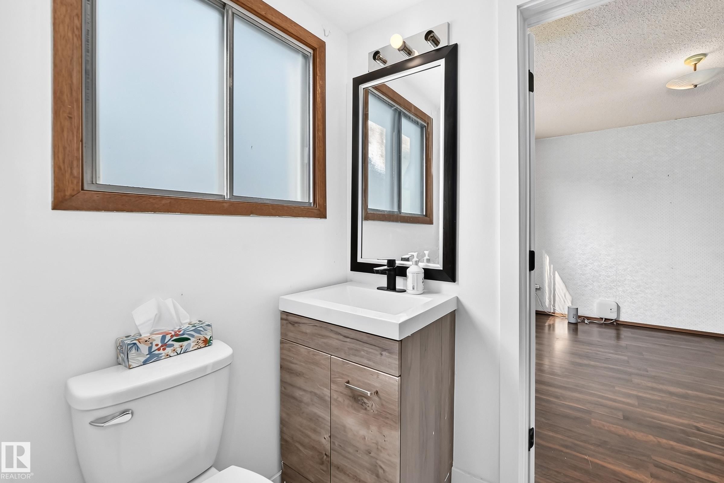 Compact bathroom featuring a wood-finish vanity with a white countertop and a contemporary black faucet - 1928 68 Street Nw, Edmonton, AB - Indoor Photo Showing Bathroom