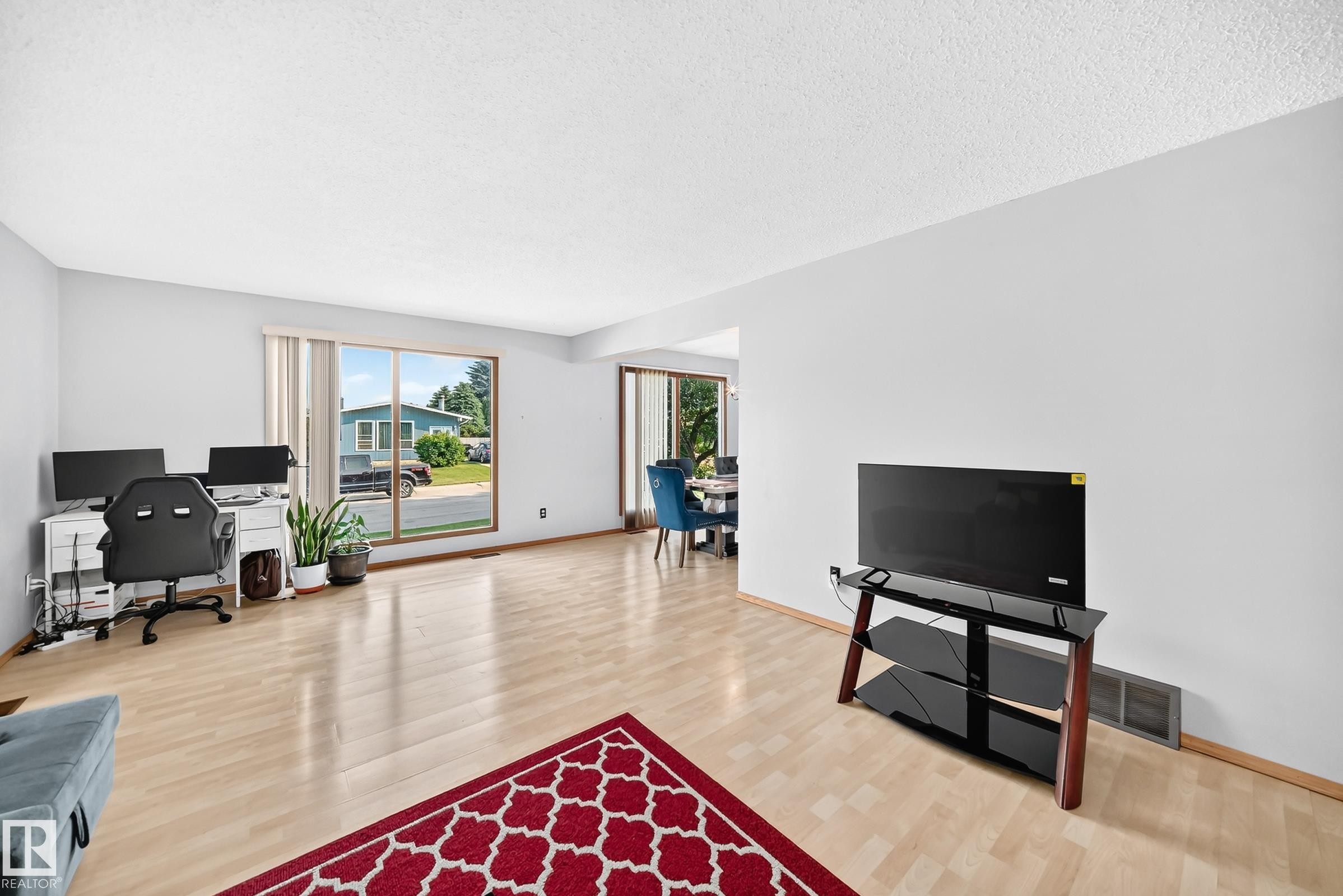 Spacious main living area featuring light wood-finish flooring, a large picture window, light-toned walls, and an open doorway to an additional room - 1928 68 Street Nw, Edmonton, AB - Indoor Photo Showing Living Room