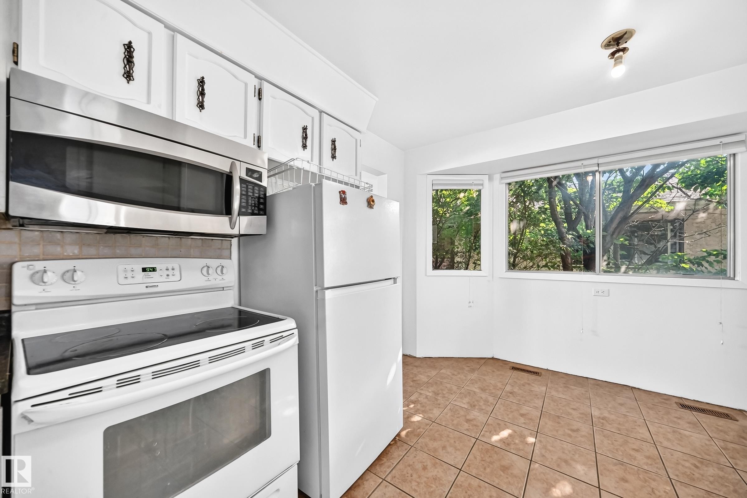 Kitchen featuring white cabinetry with decorative hardware, a stainless steel over-the-range microwave, and a white electric range - 1928 68 Street Nw, Edmonton, AB - Indoor Photo Showing Kitchen