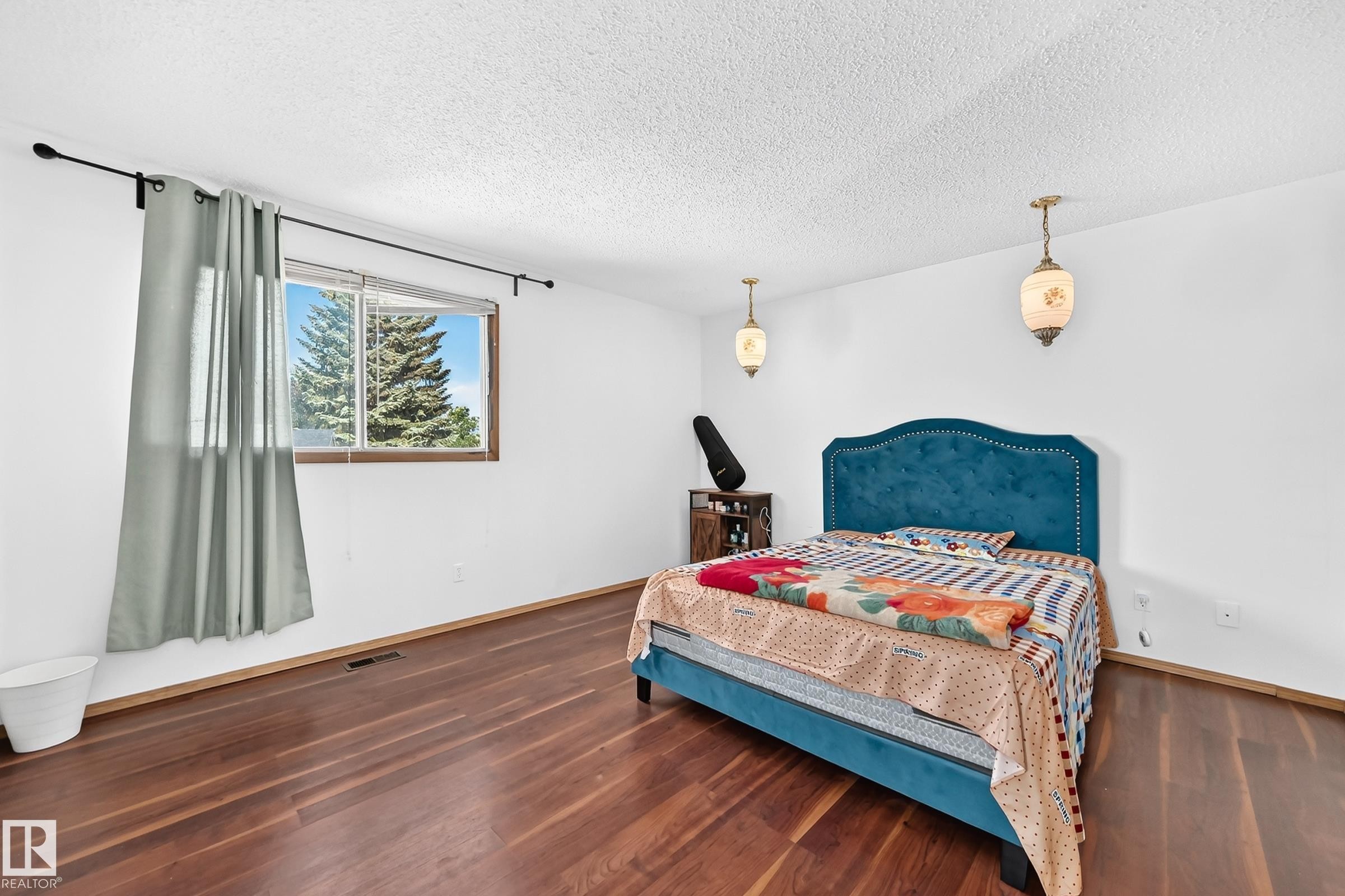 Bedroom featuring wood-finish flooring, white walls, and a window with a green tree backdrop - 1928 68 Street Nw, Edmonton, AB - Indoor Photo Showing Bedroom