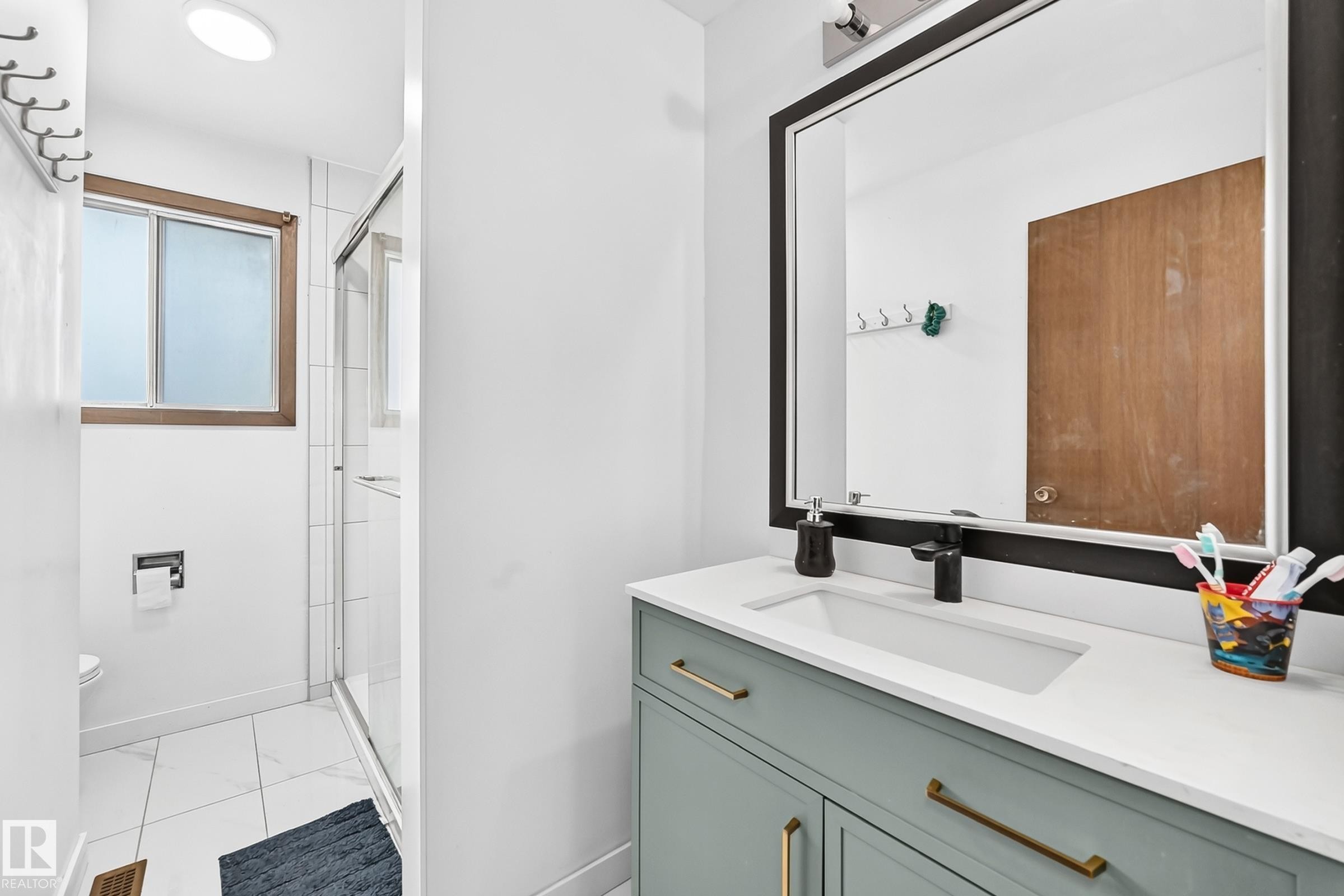 Modern bathroom featuring a mint green vanity with gold-tone hardware, a rectangular undermount sink, and a black-framed mirror - 1928 68 Street Nw, Edmonton, AB - Indoor Photo Showing Bathroom