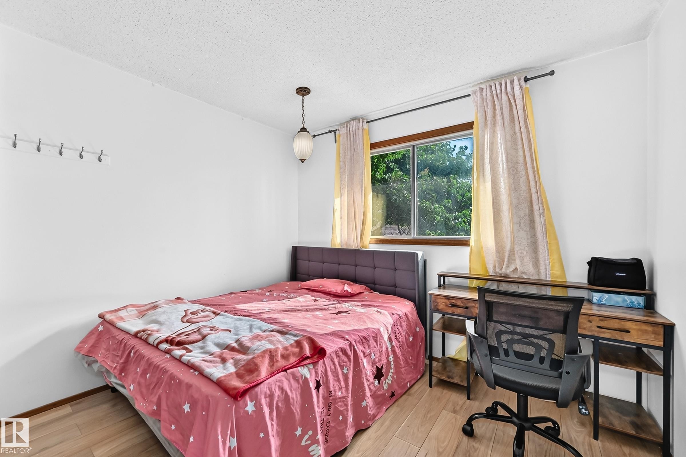 Room featuring wood-finish flooring, a pendant light fixture, a window with exterior views, and a wall-mounted coat rack - 1928 68 Street Nw, Edmonton, AB - Indoor Photo Showing Bedroom