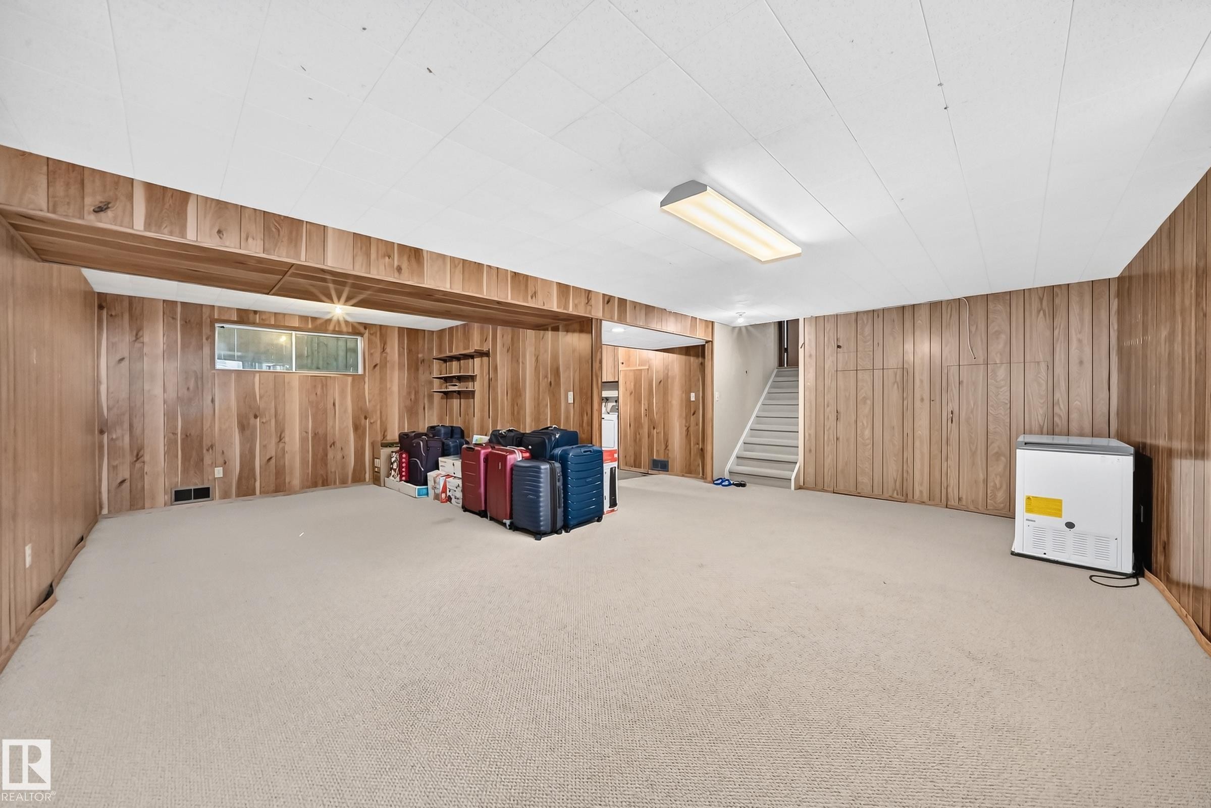 Spacious room featuring wood paneling, light-colored carpeting, and a drop ceiling with fluorescent lighting - 1928 68 Street Nw, Edmonton, AB - Indoor