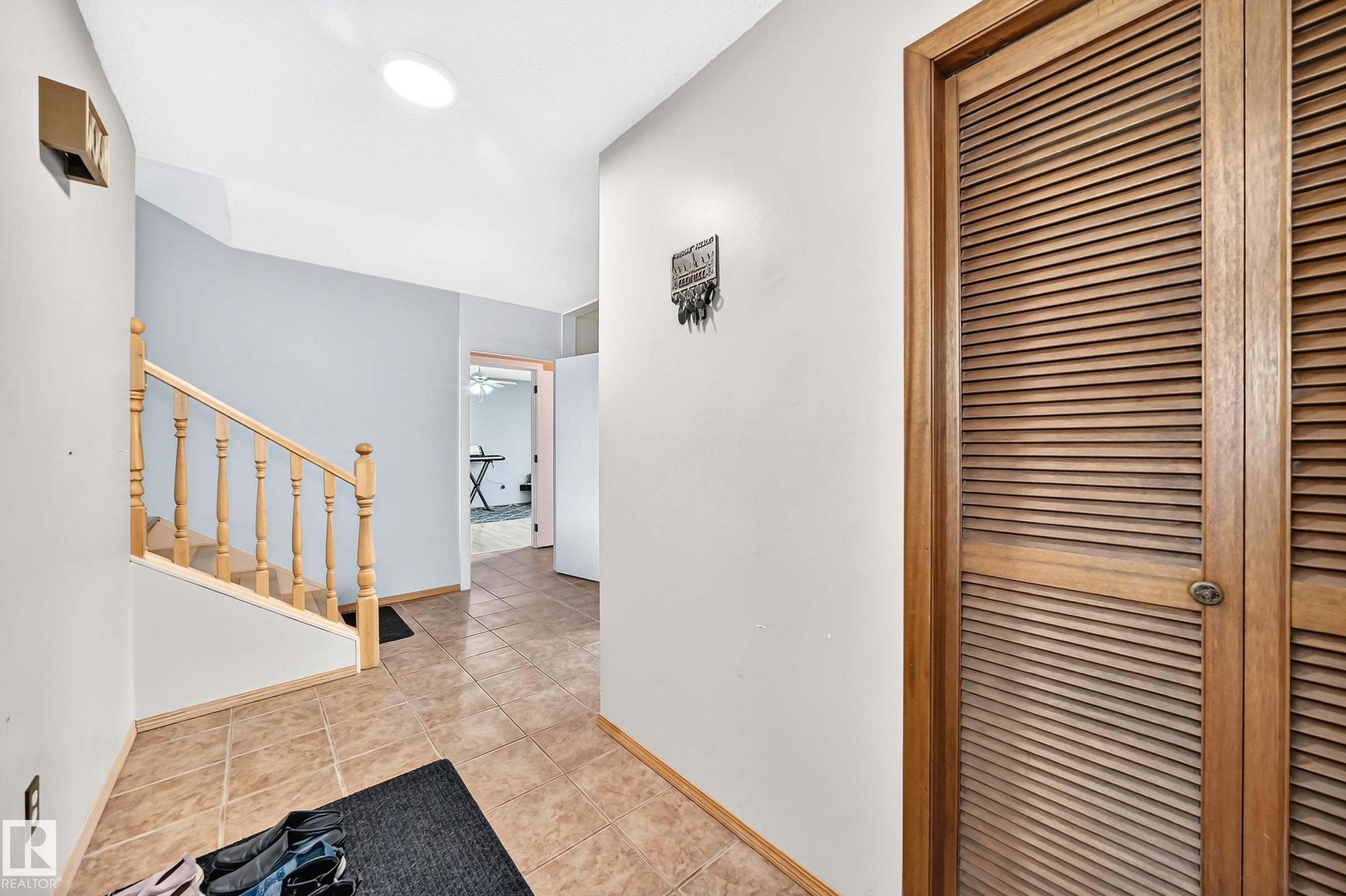 Foyer with neutral tile flooring, wood-finish staircase with balusters, louvered bi-fold closet doors, and recessed ceiling lighting - 1928 68 Street Nw, Edmonton, AB - Indoor Photo Showing Other Room