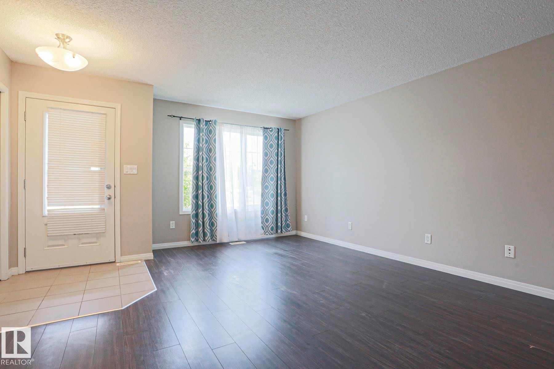 Spacious room featuring dark wood-finish flooring, light neutral wall paint, and white trim - 489 Orchards Boulevard Sw, Edmonton, AB - Indoor Photo Showing Other Room