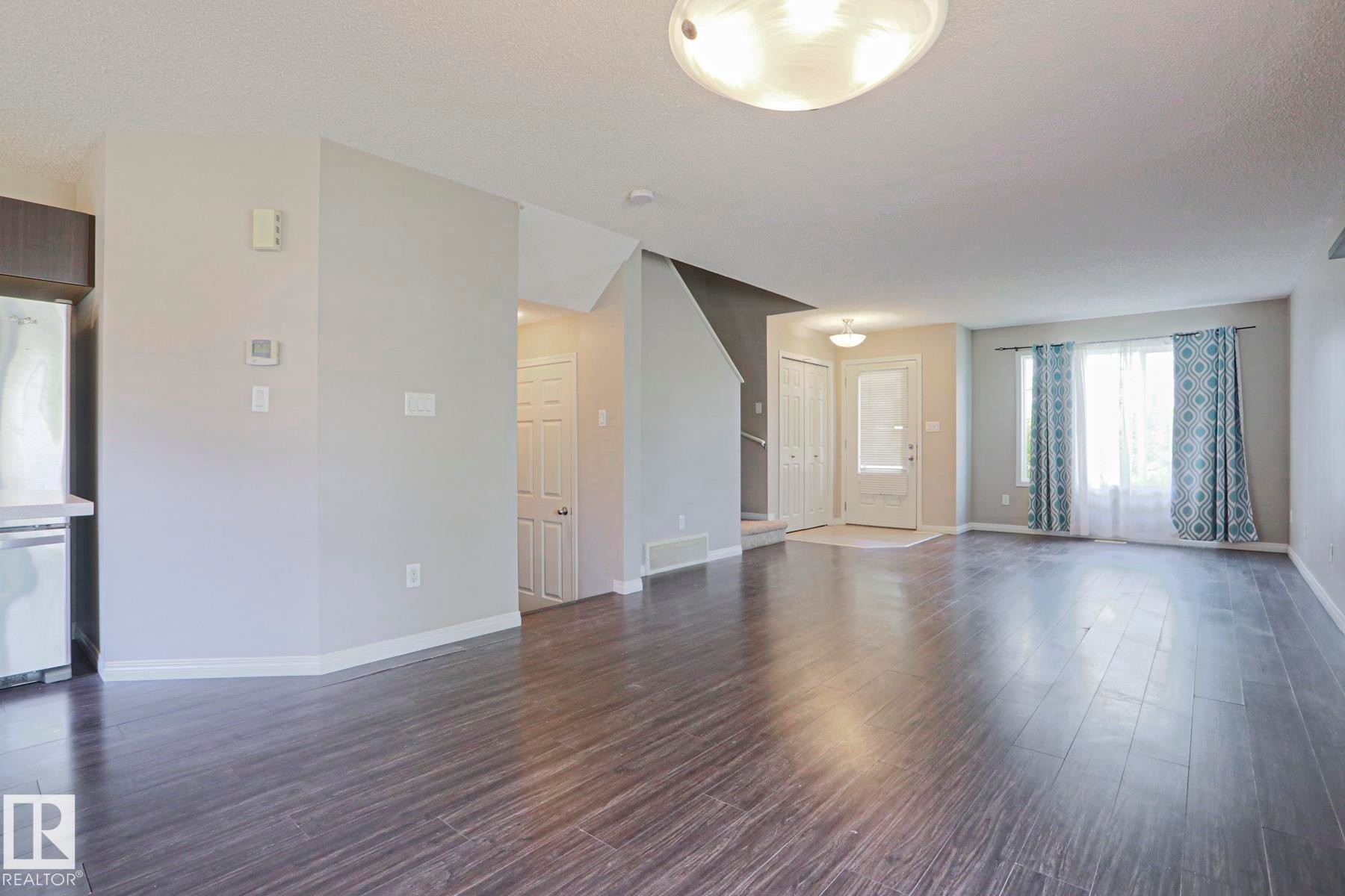 Spacious living area featuring dark wood-finish flooring and light gray painted walls - 489 Orchards Boulevard Sw, Edmonton, AB - Indoor Photo Showing Other Room