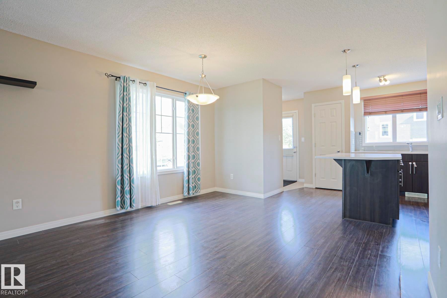 Open-concept living area with dark wood-finish flooring, a contemporary pendant light fixture, and a large window providing natural light - 489 Orchards Boulevard Sw, Edmonton, AB - Indoor