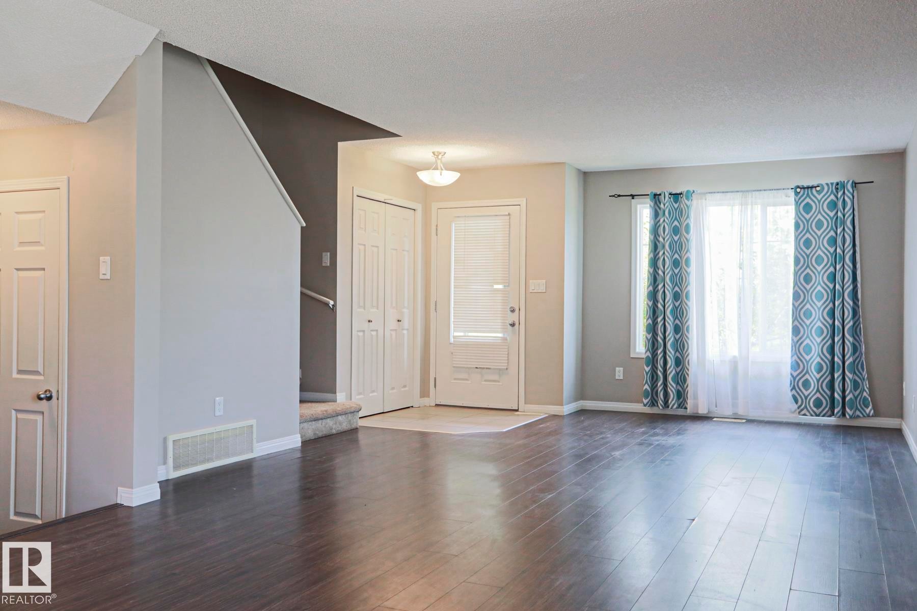 Spacious living area featuring wood-finish flooring, ample natural light from large windows, and a neutral color palette - 489 Orchards Boulevard Sw, Edmonton, AB - Indoor Photo Showing Other Room