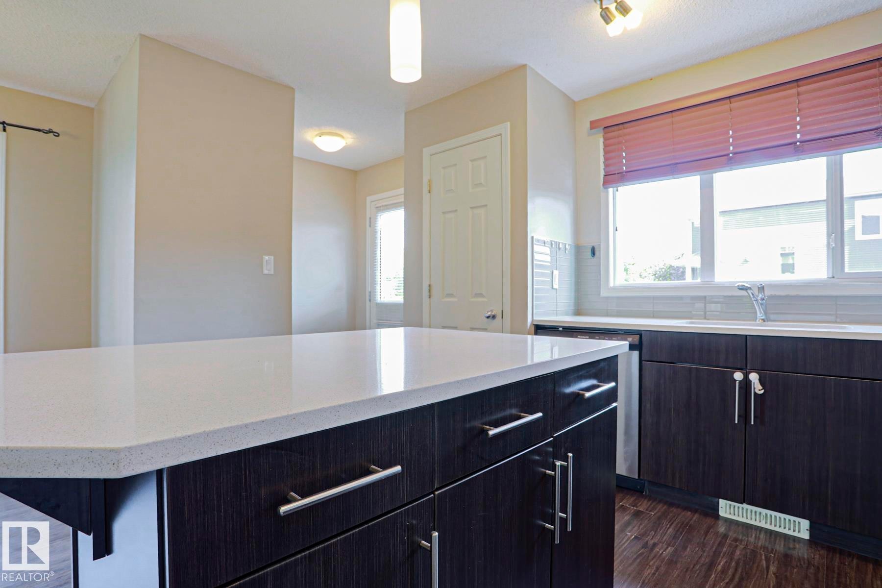 Kitchen island featuring a light-toned countertop, dark wood-finish cabinetry, and stainless steel hardware - 489 Orchards Boulevard Sw, Edmonton, AB - Indoor Photo Showing Other Room