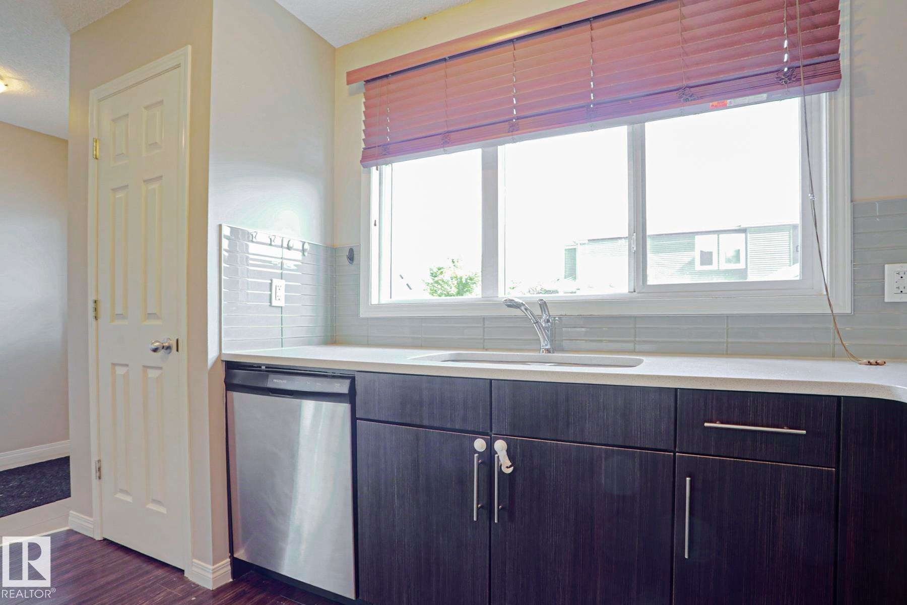 Kitchen area featuring dark wood-finish cabinetry, a stainless steel dishwasher, and a white countertop with an integrated sink - 489 Orchards Boulevard Sw, Edmonton, AB - Indoor Photo Showing Kitchen
