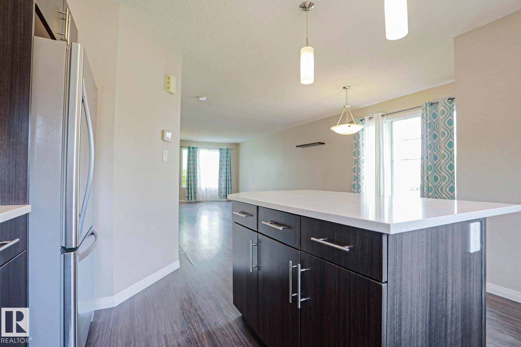 Kitchen island featuring a white countertop, dark wood-finish cabinetry, and stainless-steel hardware - 489 Orchards Boulevard Sw, Edmonton, AB - Indoor Photo Showing Kitchen