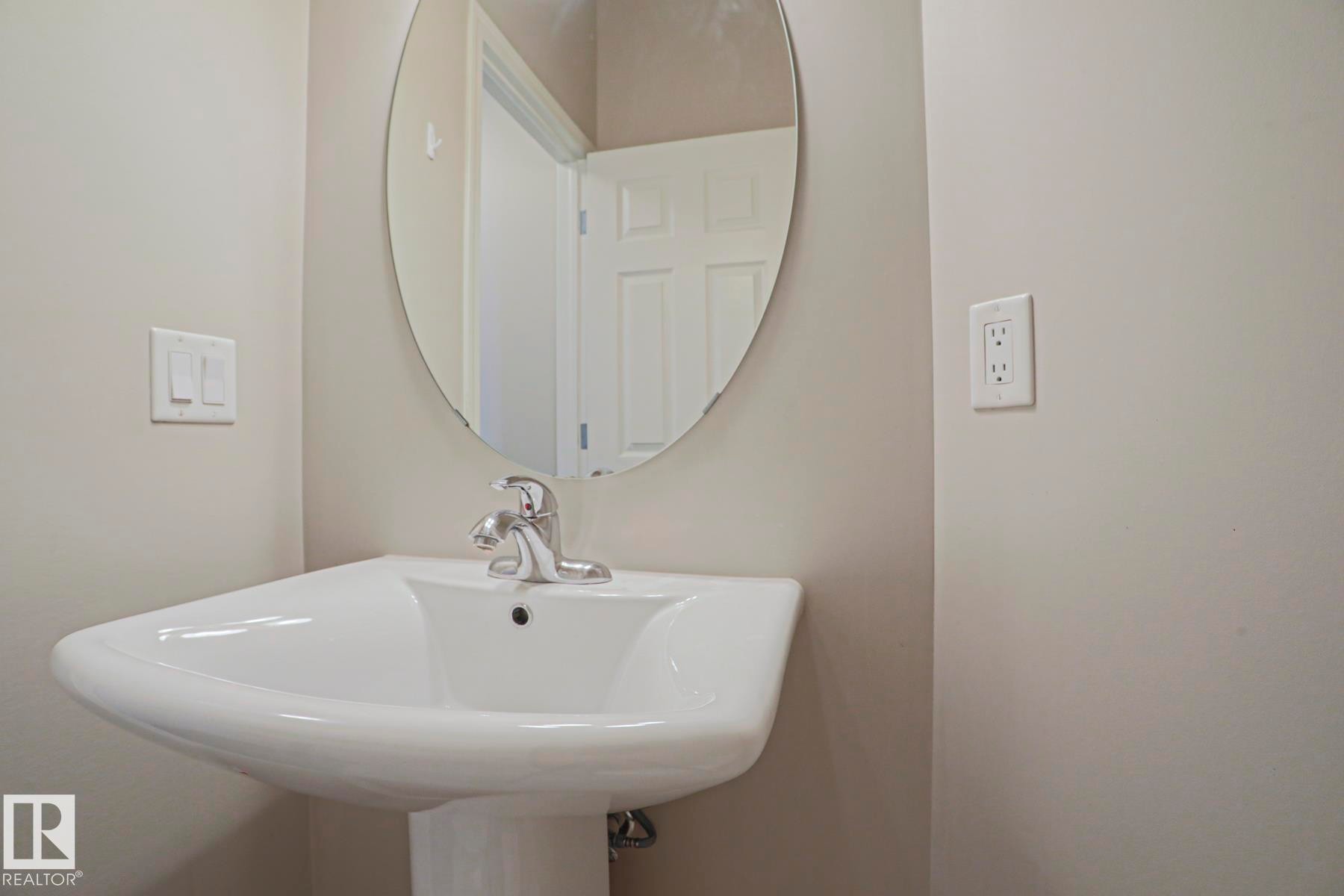 Pedestal sink with chrome faucet and an oval wall-mounted mirror - 489 Orchards Boulevard Sw, Edmonton, AB - Indoor Photo Showing Bathroom
