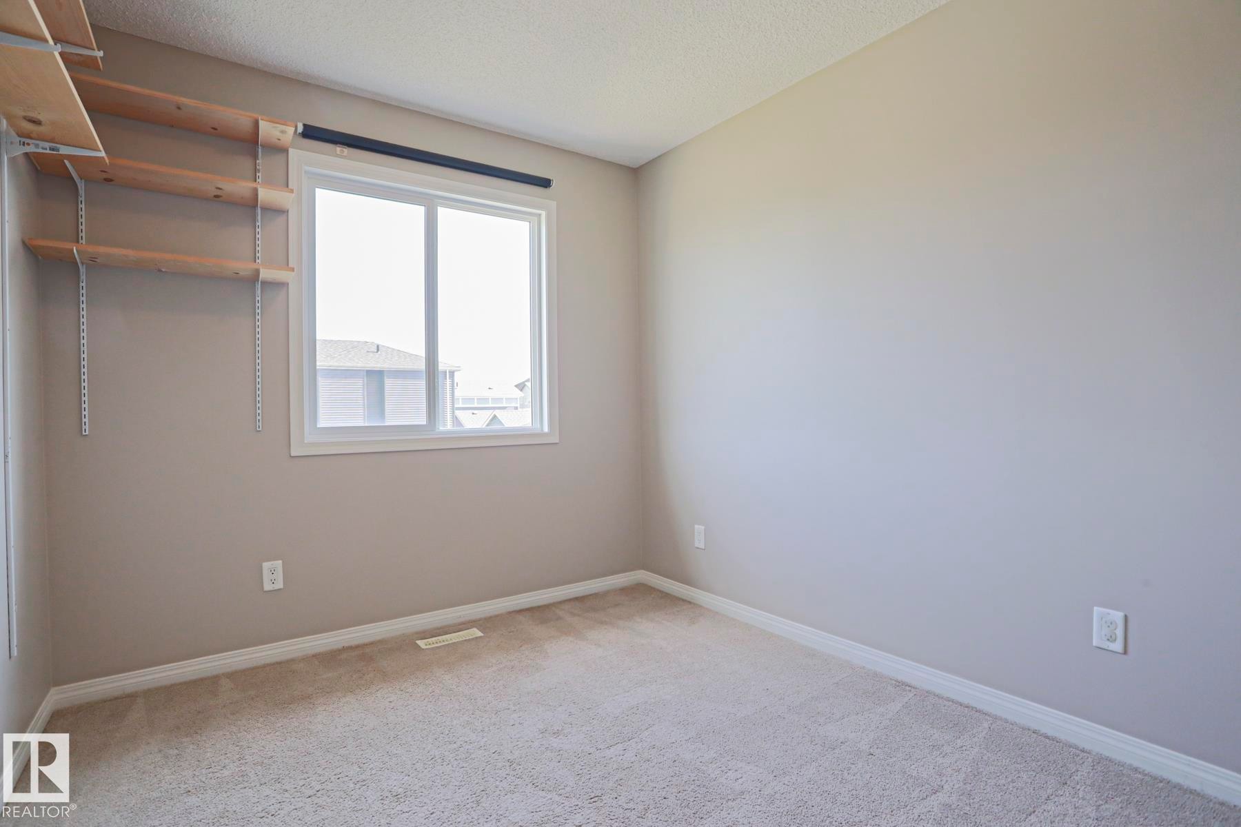 Carpeted room featuring a white-framed window, neutral painted walls, and built-in adjustable shelving - 489 Orchards Boulevard Sw, Edmonton, AB - Indoor Photo Showing Other Room