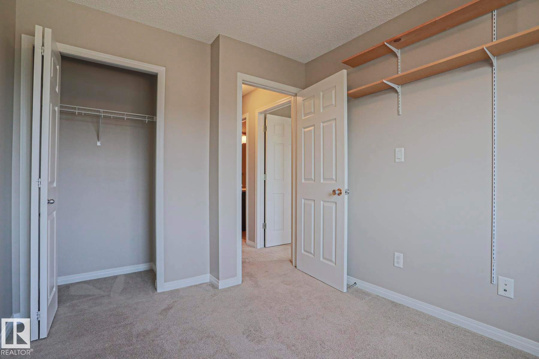 Carpeted room featuring light gray wall paint, white trim, a bi-fold closet with wire shelving, and adjustable wall-mounted shelving - 489 Orchards Boulevard Sw, Edmonton, AB - Indoor Photo Showing Other Room