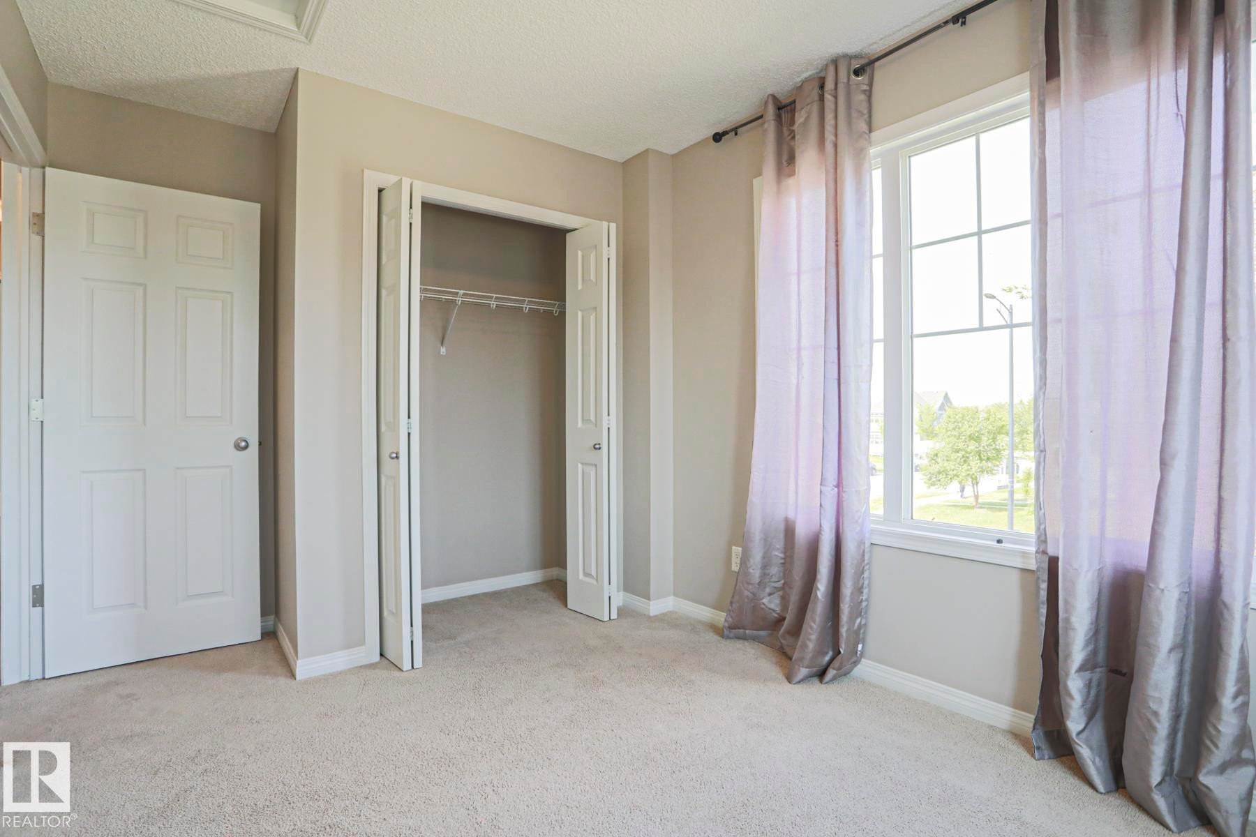 Carpeted room featuring a large window with grid panes, a bi-fold closet, a six-panel door, and neutral wall paint - 489 Orchards Boulevard Sw, Edmonton, AB - Indoor