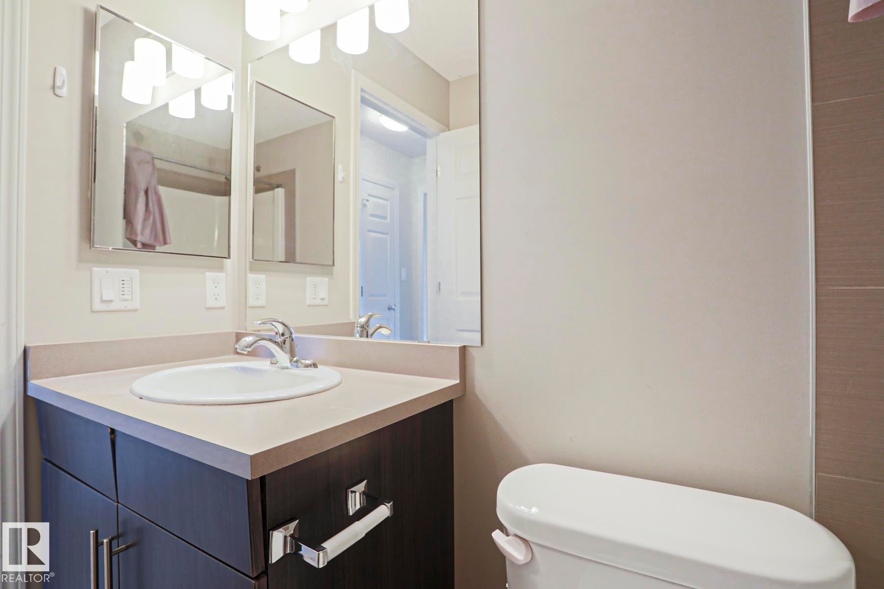 Bathroom vanity featuring an integrated sink, polished chrome faucet, and dark wood-finish cabinetry - 489 Orchards Boulevard Sw, Edmonton, AB - Indoor Photo Showing Bathroom