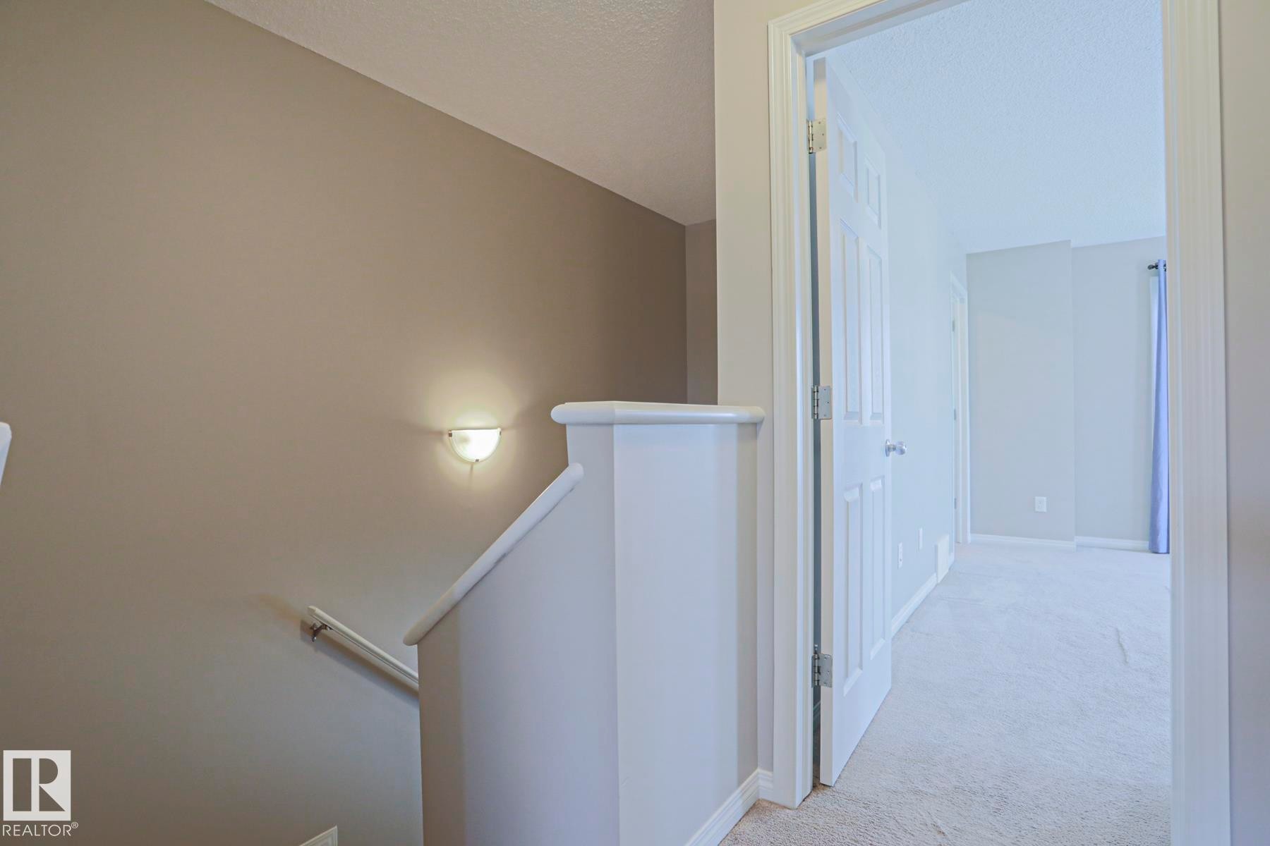 Carpeted hallway with a neutral wall palette, a built-in wall sconce, and white trim - 489 Orchards Boulevard Sw, Edmonton, AB - Indoor Photo Showing Other Room