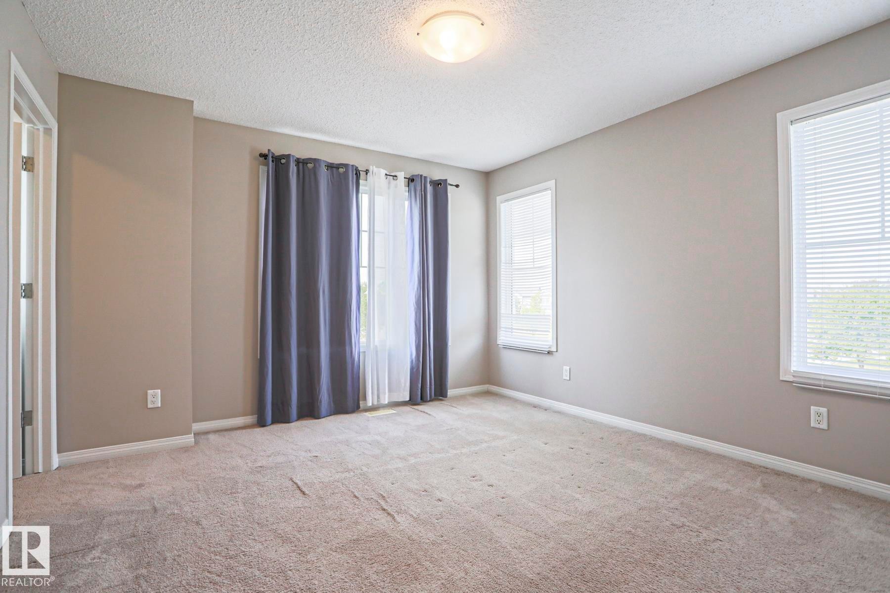 Spacious room featuring neutral paint tones, multiple windows with blinds, and light-colored carpet flooring - 489 Orchards Boulevard Sw, Edmonton, AB - Indoor Photo Showing Other Room