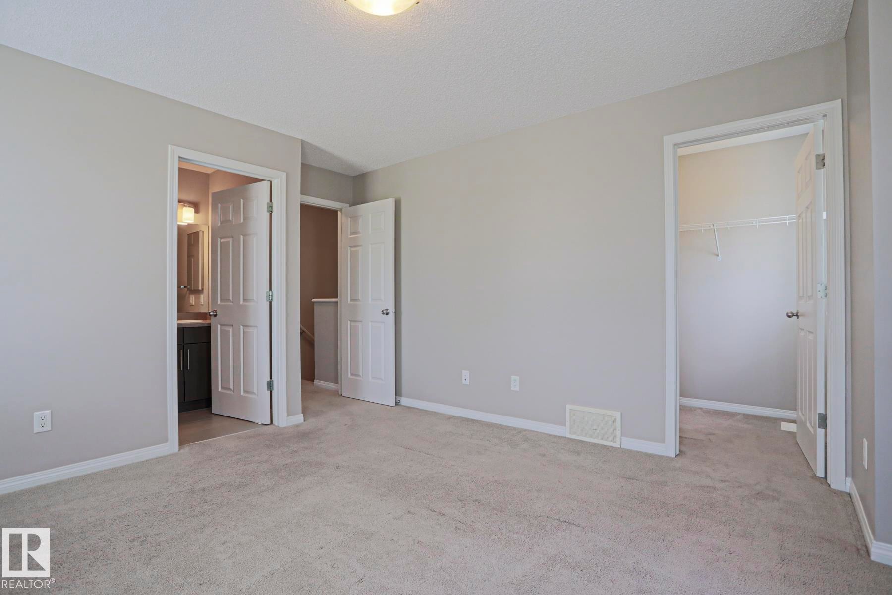 Carpeted room with light neutral wall paint, featuring a standard closet with wire shelving and a vanity area with a dark cabinet and wall-mounted light fixture - 489 Orchards Boulevard Sw, Edmonton, AB - Indoor