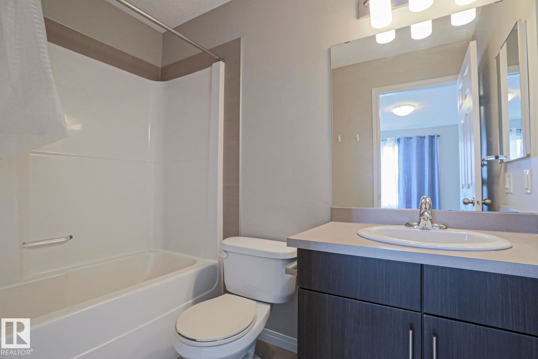 Bathroom featuring a white bathtub, toilet, and vanity with an integrated sink and base cabinetry - 489 Orchards Boulevard Sw, Edmonton, AB - Indoor Photo Showing Bathroom
