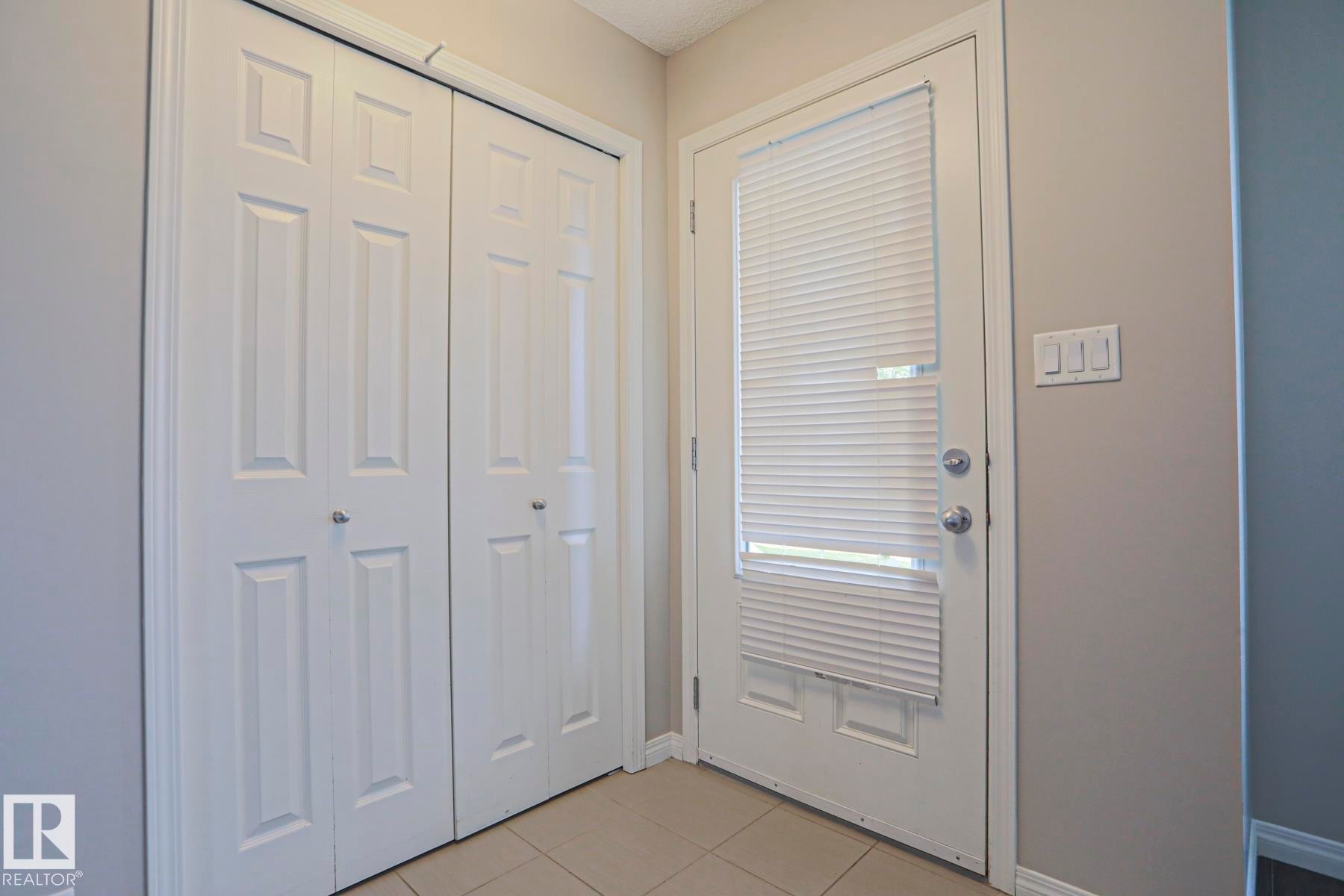 Entryway featuring a white paneled door with integrated cellular blinds, light beige wall paint, tile flooring, and a multi-panel closet door - 489 Orchards Boulevard Sw, Edmonton, AB - Indoor Photo Showing Other Room
