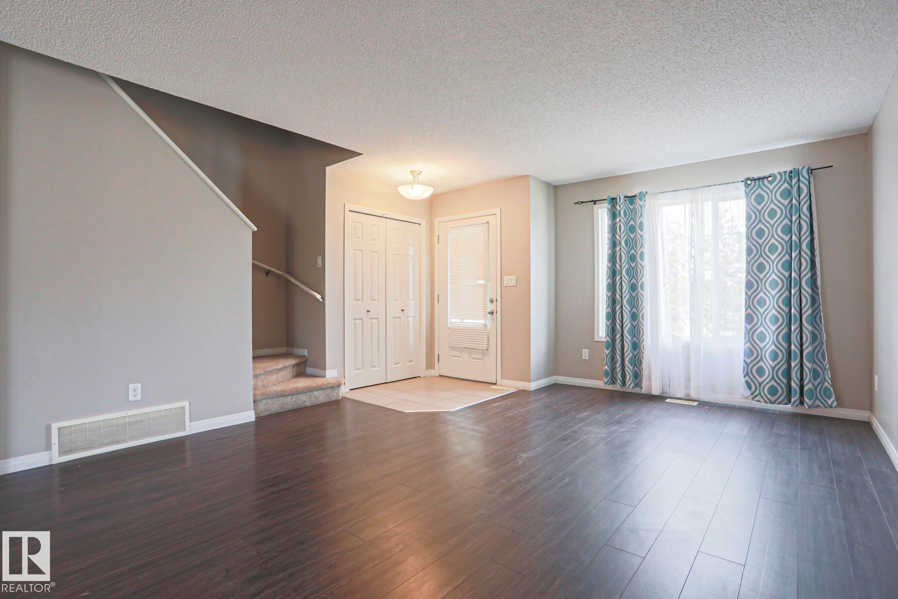 Living area with dark wood-finish flooring, a front entrance with a light-colored tile inset, and a staircase featuring carpeted treads and a metal handrail - 489 Orchards Boulevard Sw, Edmonton, AB - Indoor Photo Showing Other Room