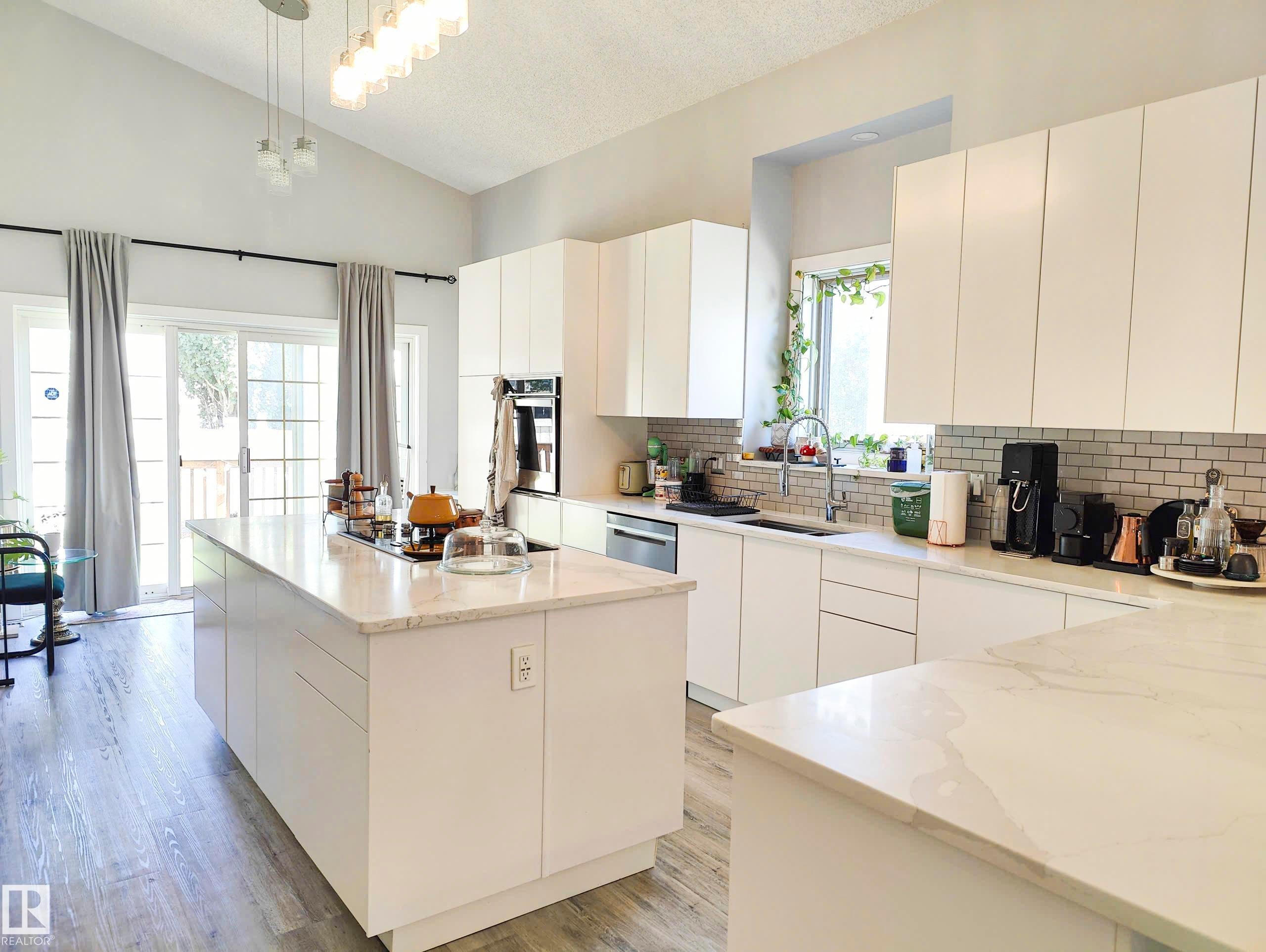 Modern kitchen featuring high vaulted ceilings, light wood-finish flooring, white flat-panel cabinetry, light-colored countertops, and a subway tile backsplash - 215 Peter Close, Edmonton, AB - Indoor Photo Showing Kitchen
