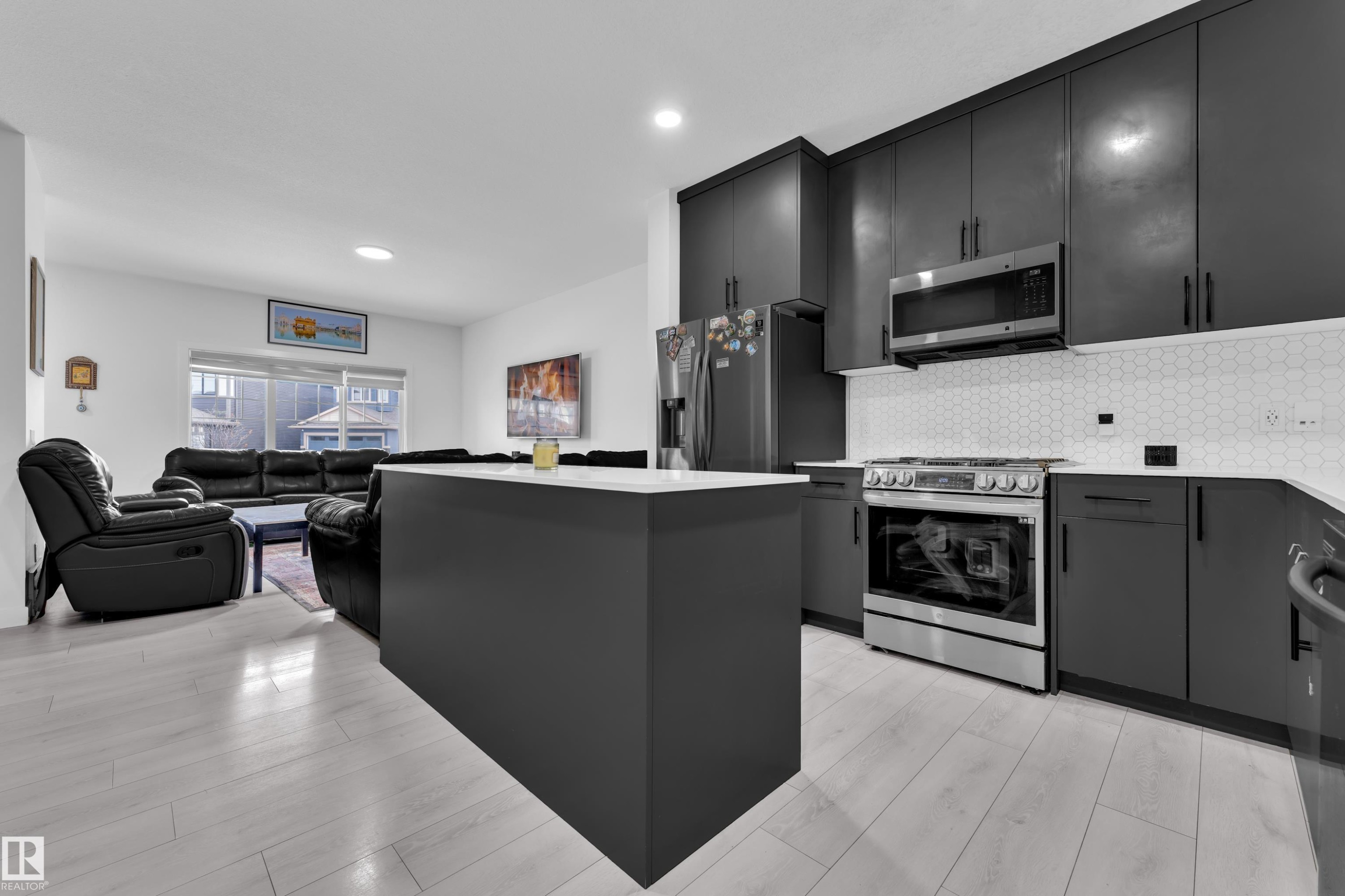 Modern kitchen featuring dark cabinetry, stainless steel appliances, white countertops, and a hexagonal tile backsplash - 1645 Plum Circle Circle Sw, Edmonton, AB - Indoor Photo Showing Kitchen
