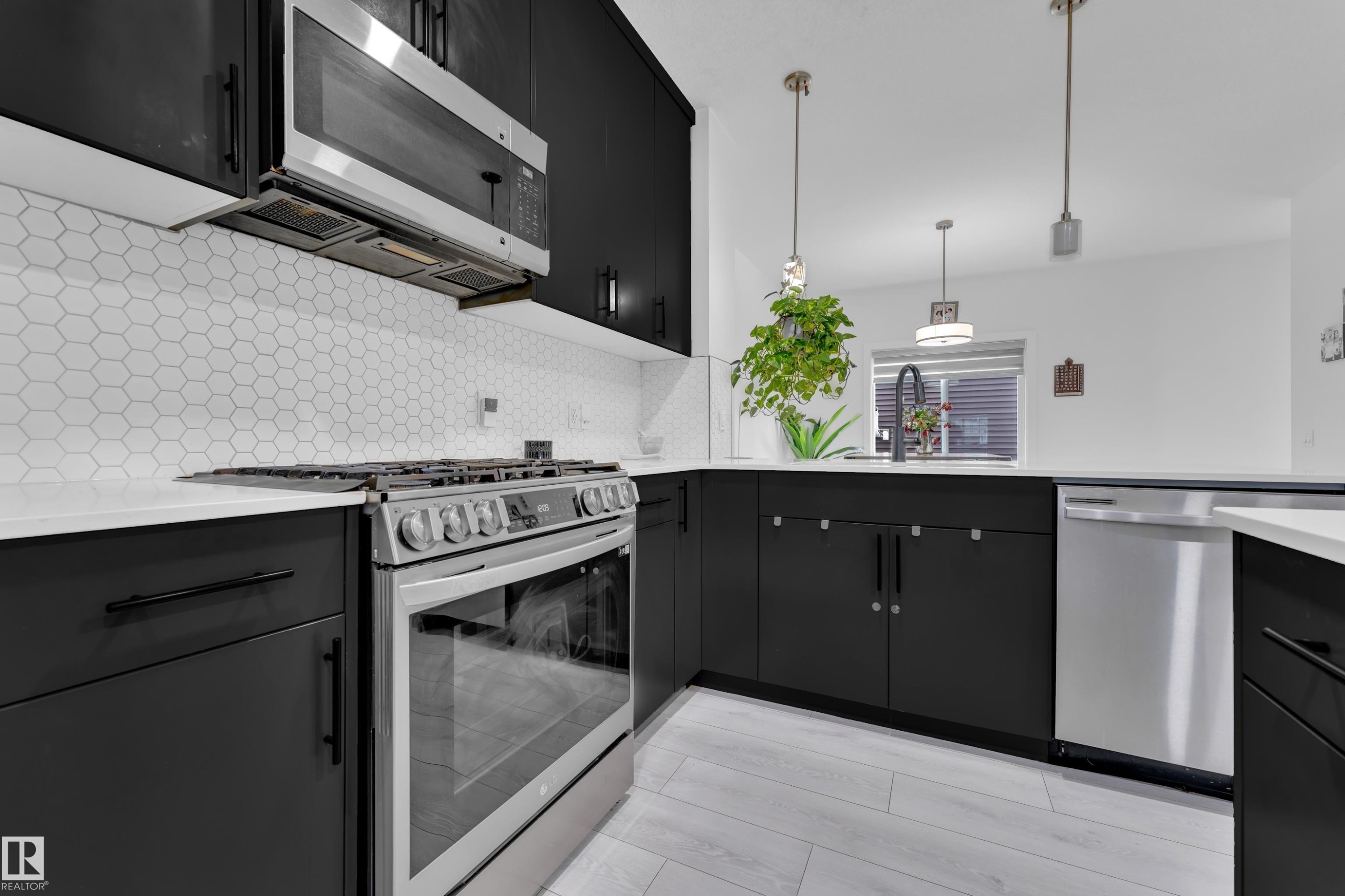 Modern kitchen featuring black cabinetry, white countertops, a hexagonal tile backsplash, stainless steel appliances, and wood-finish flooring - 1645 Plum Circle Circle Sw, Edmonton, AB - Indoor Photo Showing Kitchen With Upgraded Kitchen