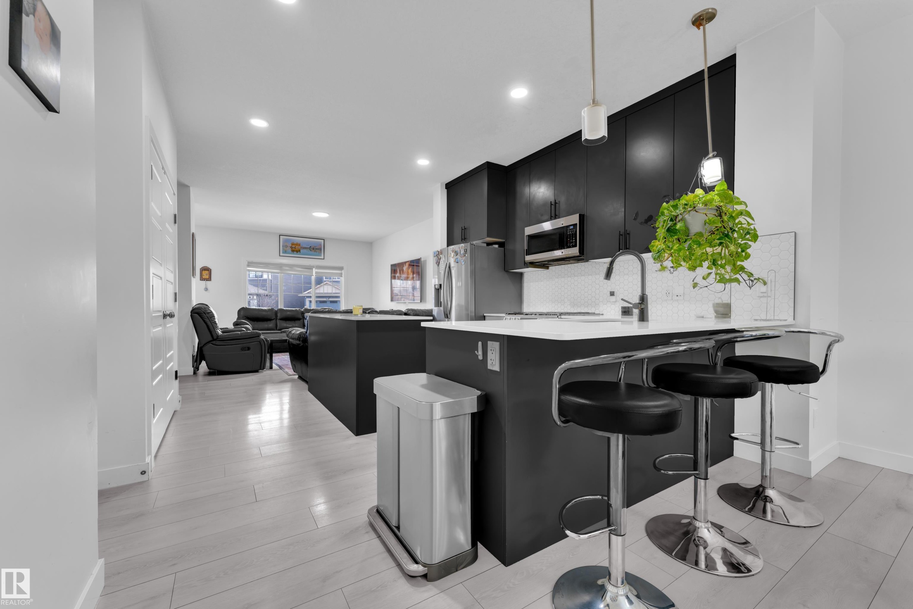 Open-concept kitchen featuring dark cabinetry, white countertops, a mosaic tile backsplash, and light wood-finish flooring - 1645 Plum Circle Circle Sw, Edmonton, AB - Indoor Photo Showing Kitchen With Upgraded Kitchen